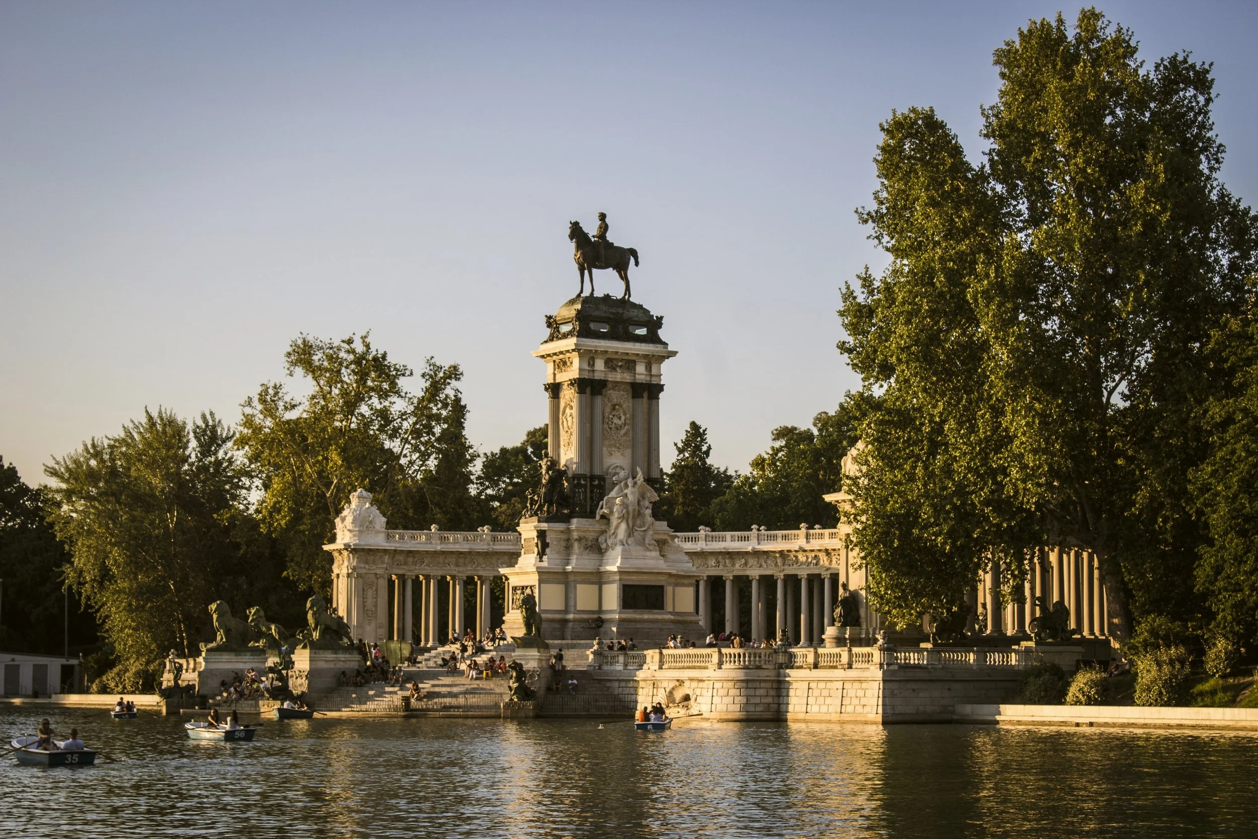 Alfonso XII Monument reflected in the Retiro pond with rowing boats at golden hour, Madrid