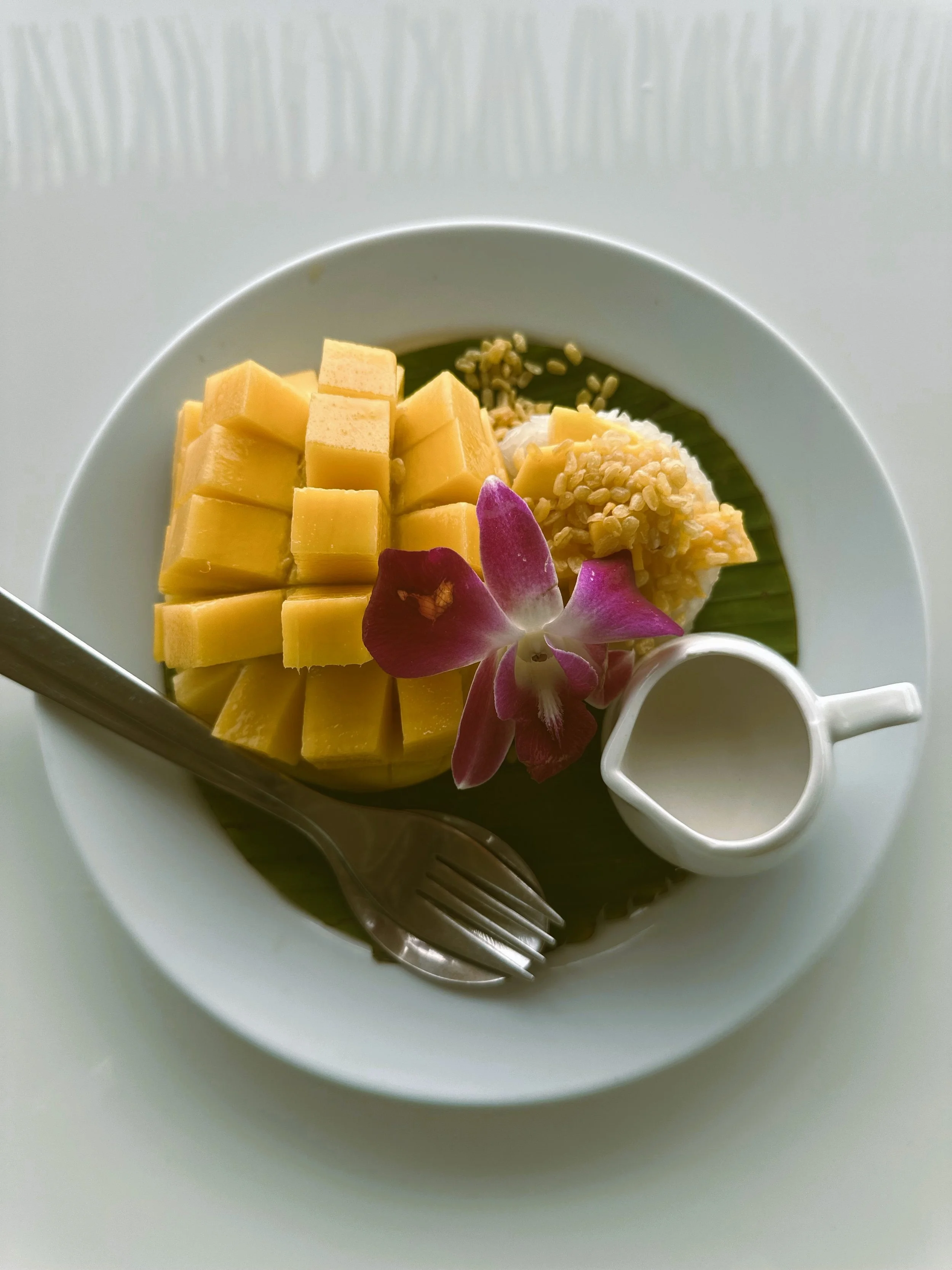 Plate of mango sticky rice with sliced mango and a small cup of coconut cream, Bangkok