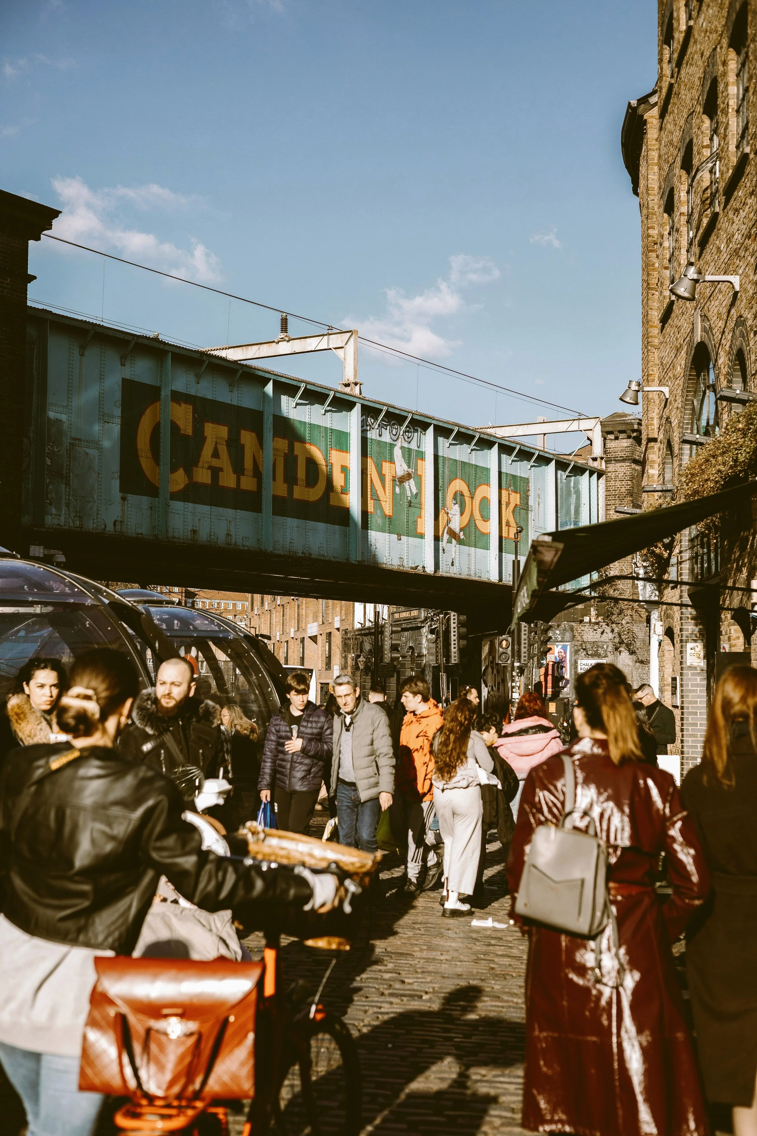 Crowded market street beneath a footbridge at Camden Lock, London.