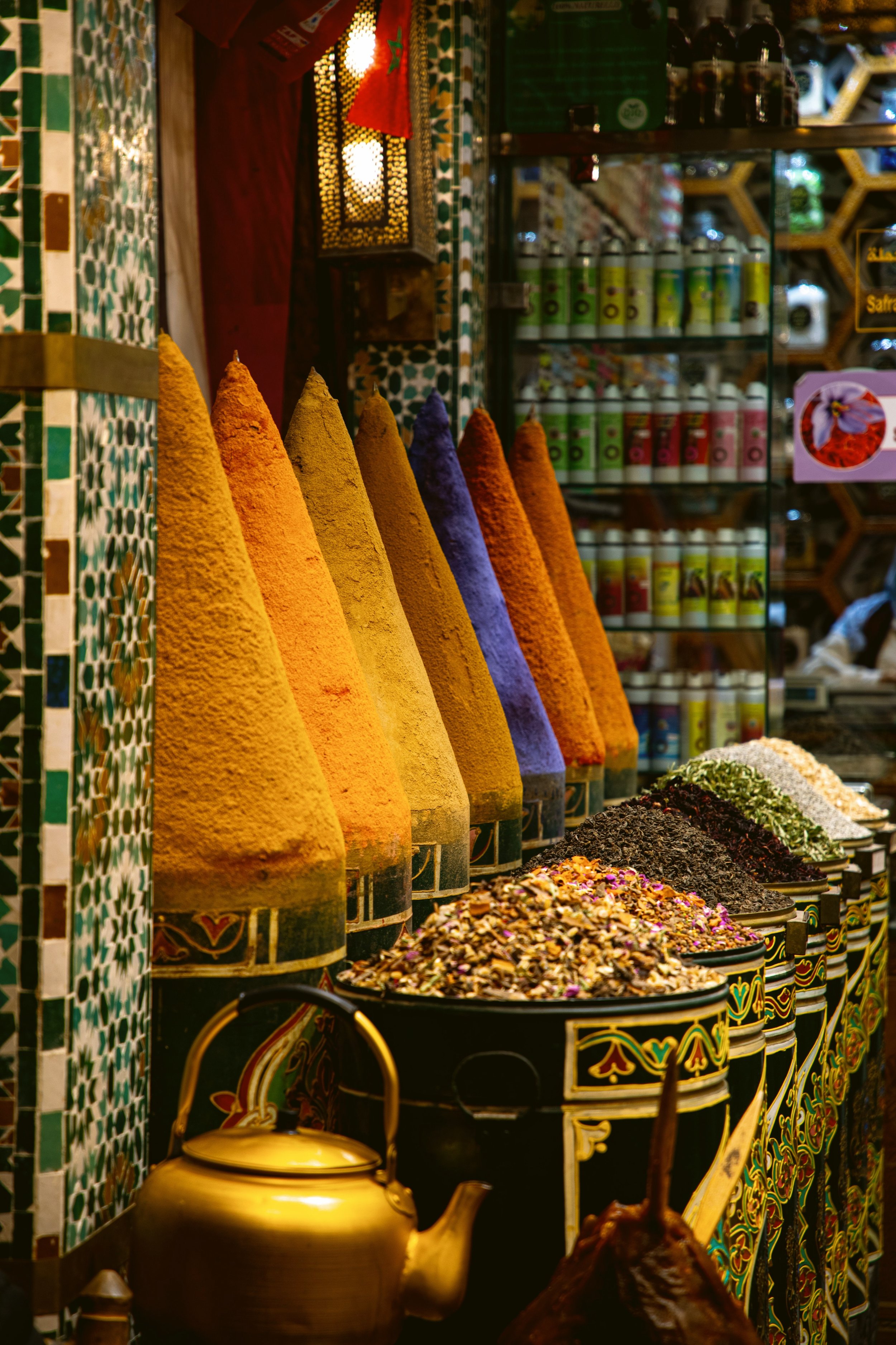 Souk stall with hanging fabrics, a brass teapot and lanterns in warm light, Marrakech.
