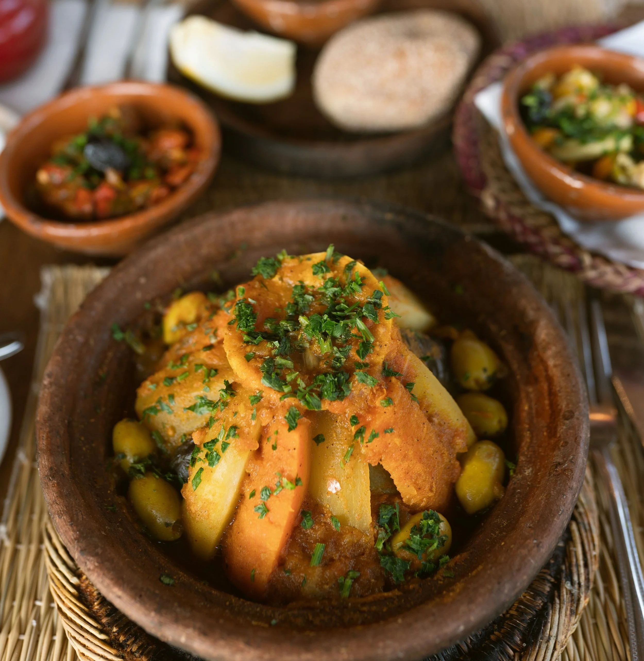 Tagine with olives and preserved lemon served in a clay dish, surrounded by small salad plates, Marrakech.