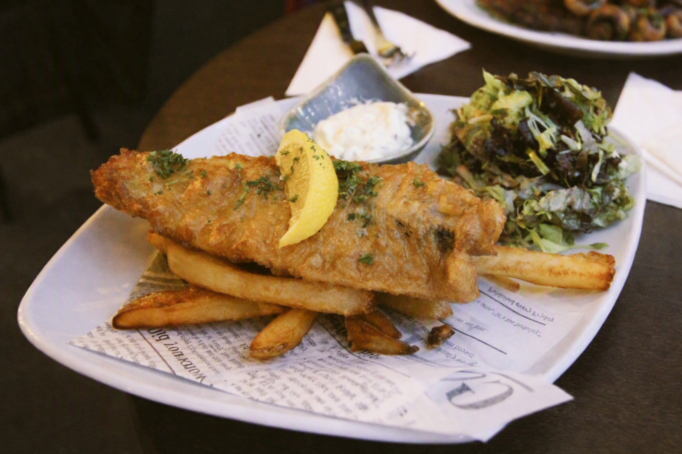 Fish and chIps served with lemon wedges, a side of tartar sauce, and a fresh garden salad on a white plate.