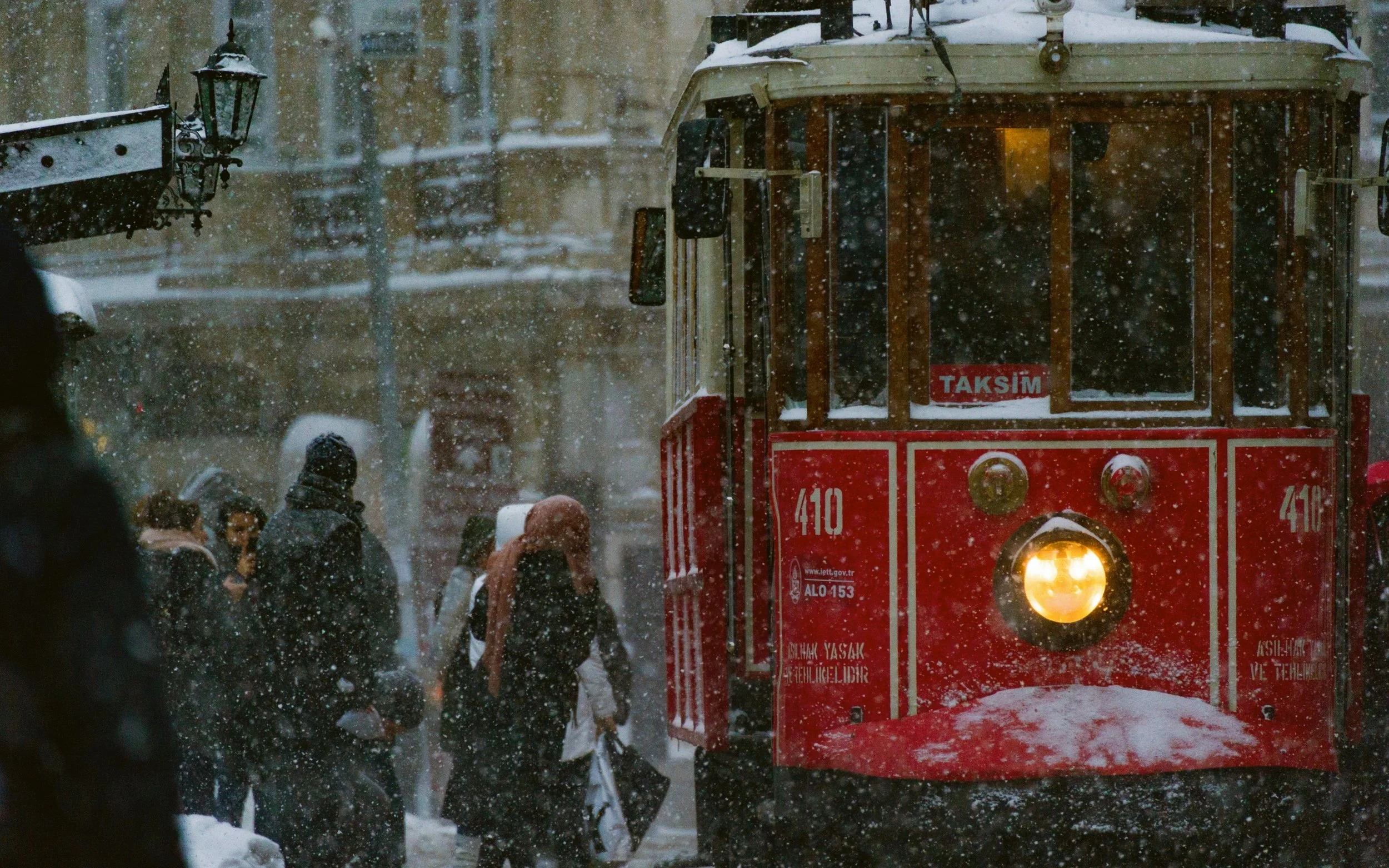 Red vintage tram passing pedestrians on a snowy day, Istiklal Avenue, Istanbul.