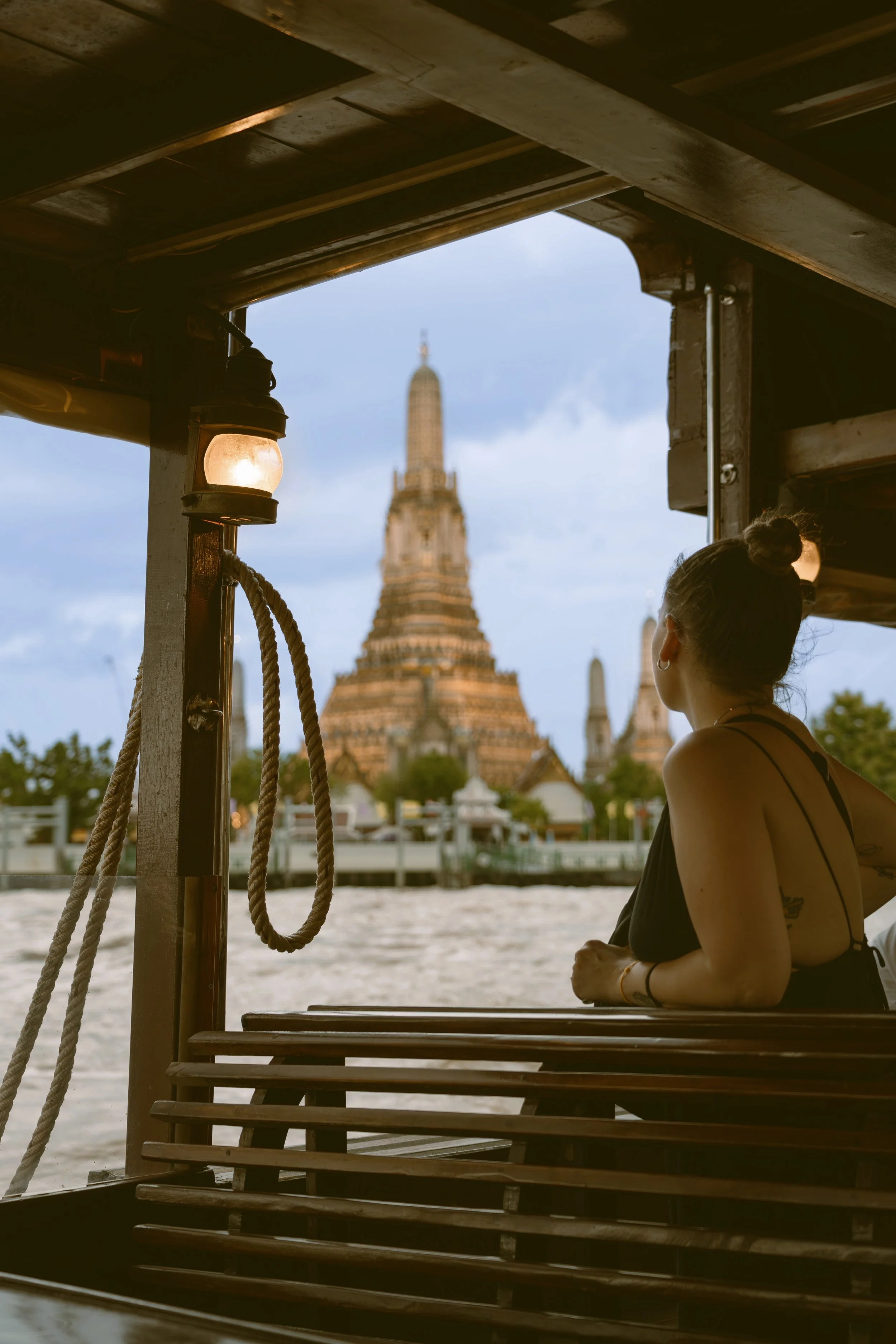 Person on a river boat looking out toward Wat Arun through the wooden frame of the deck, Bangkok.