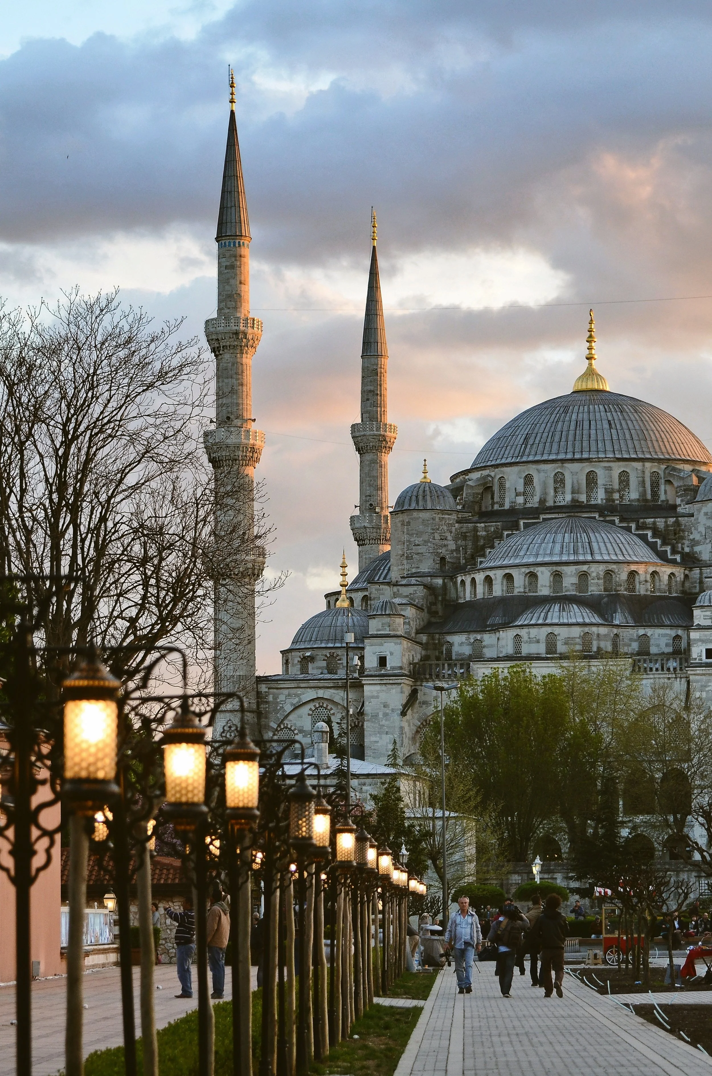 Blue Mosque with its minarets and cascading domes seen from a lamp-lit path lined with trees, Istanbul.