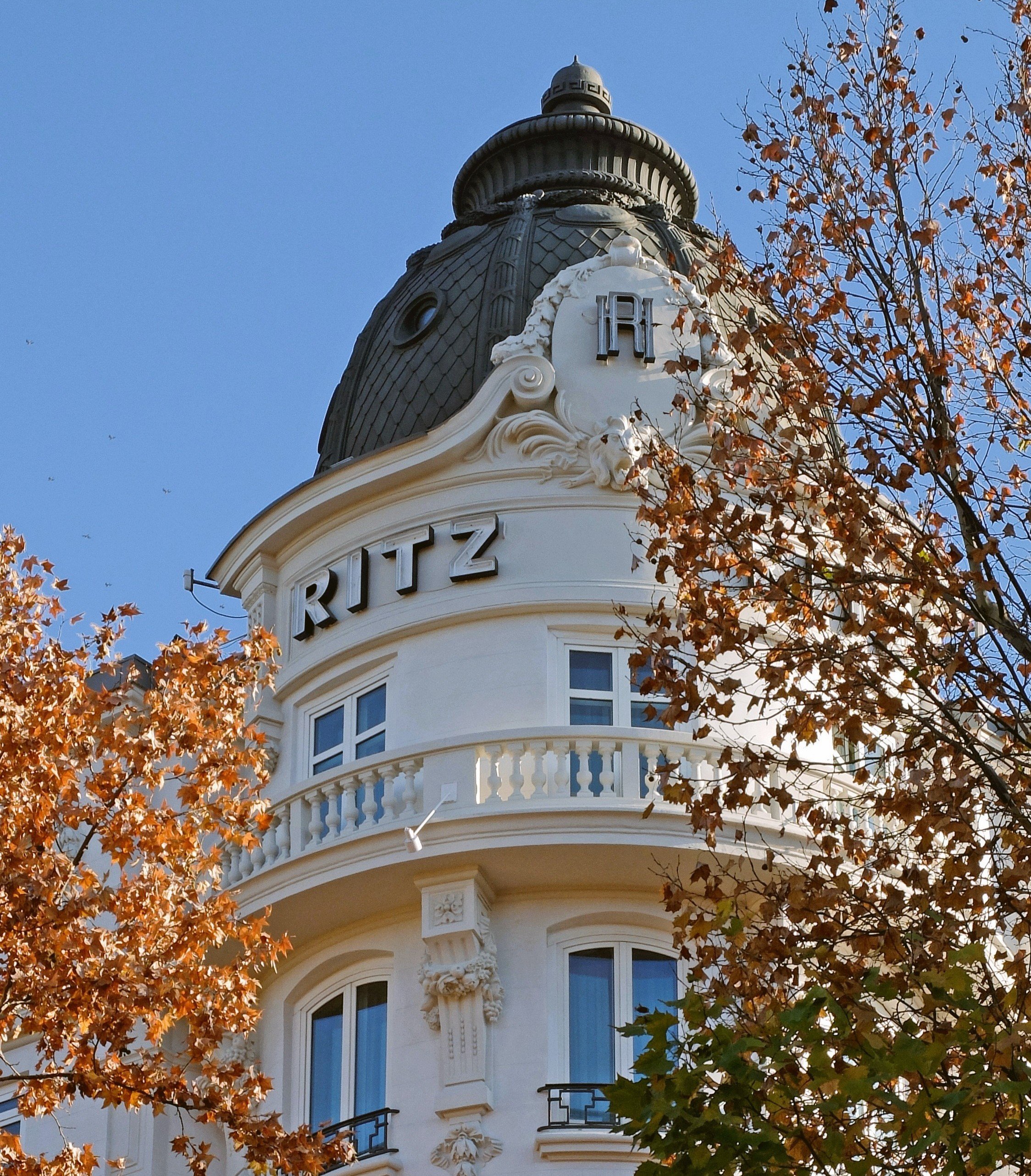 Hotel Ritz facade with curved balcony framed by autumn leaves, Madrid