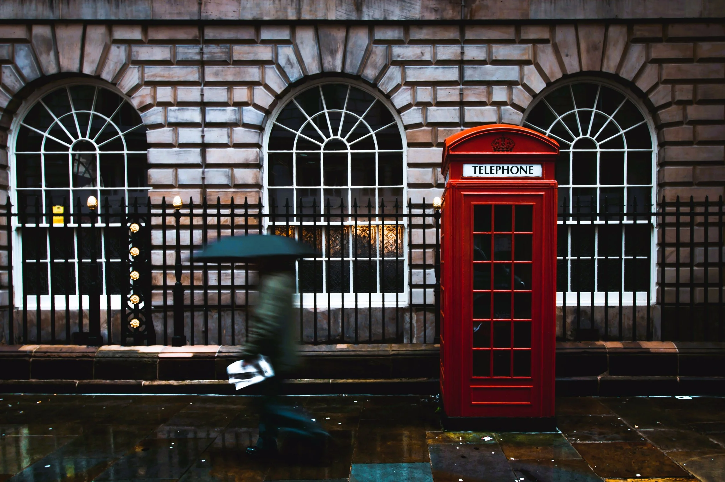 Red telephone box in front of a stone building with large arched windows, London