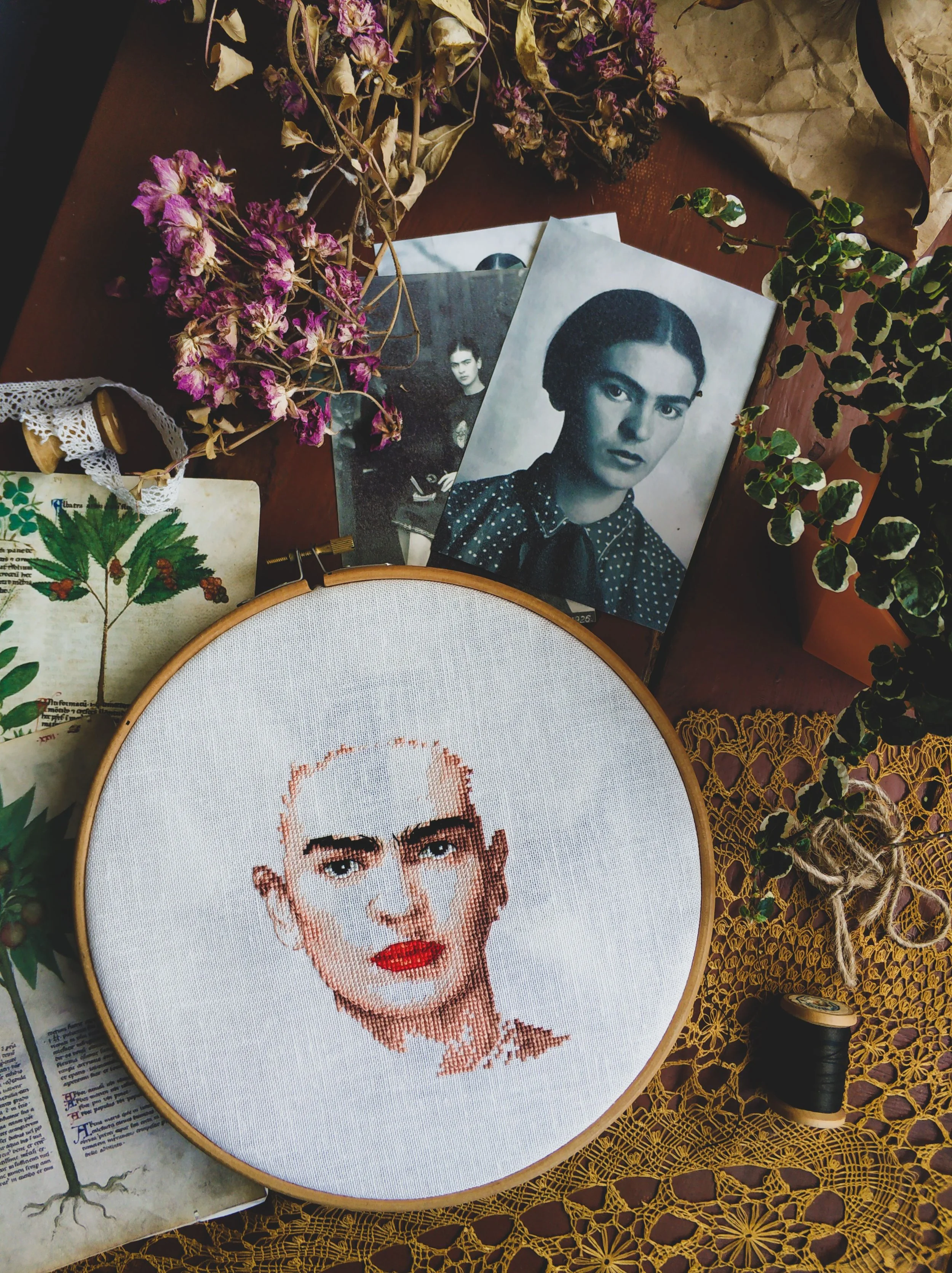 Embroidered portrait of Frida Kahlo beside a framed black-and-white photo among dried flowers and objects, Mexico City.