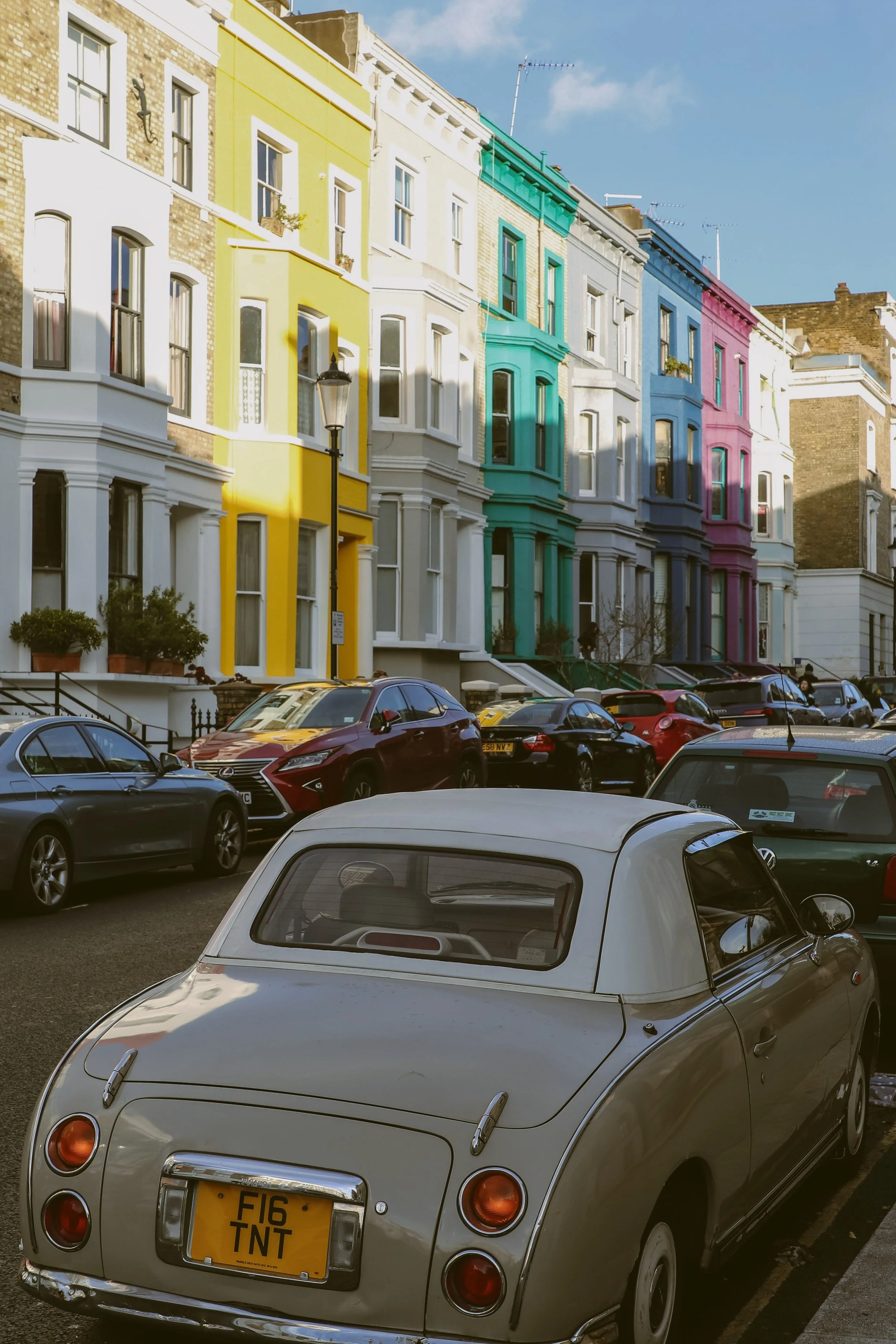 Pastel-colored townhouses lining a street with a vintage car parked in front, Notting Hill, London.