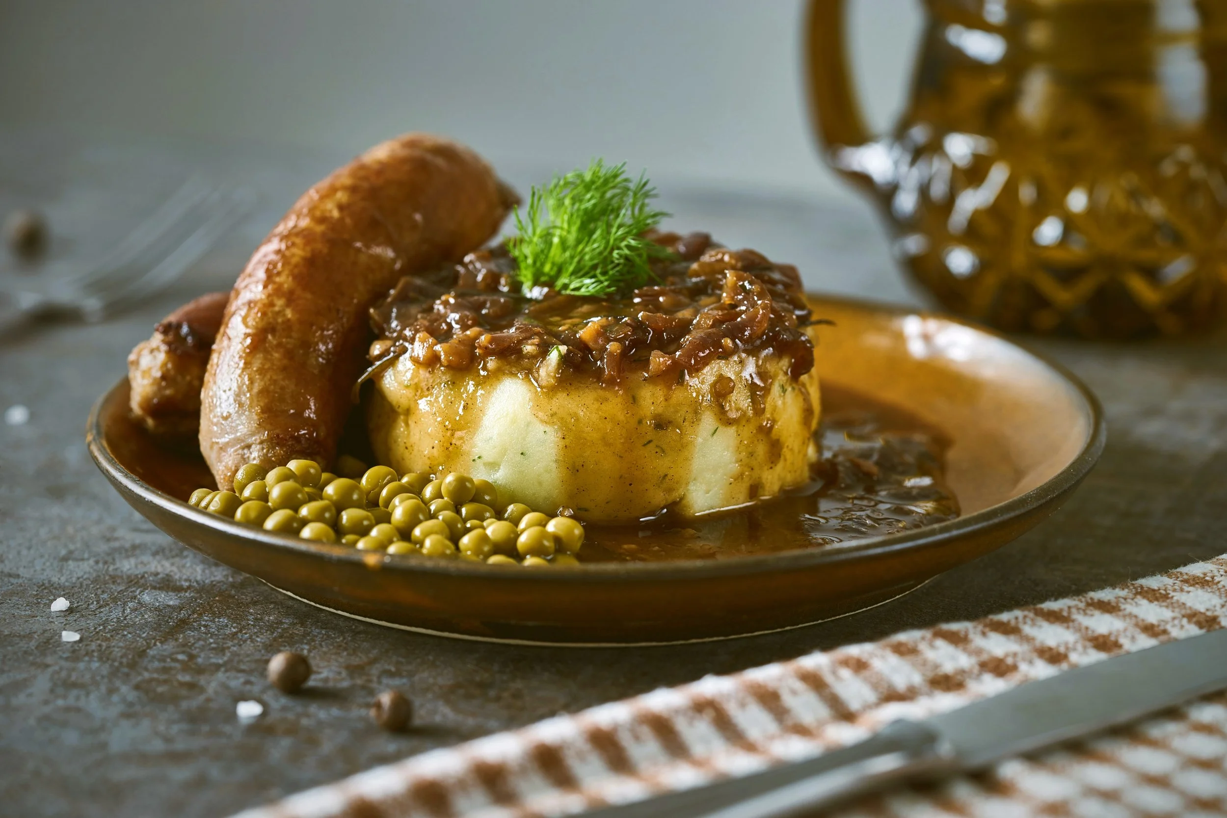 Bangers and mash with peas and gravy on a plate.