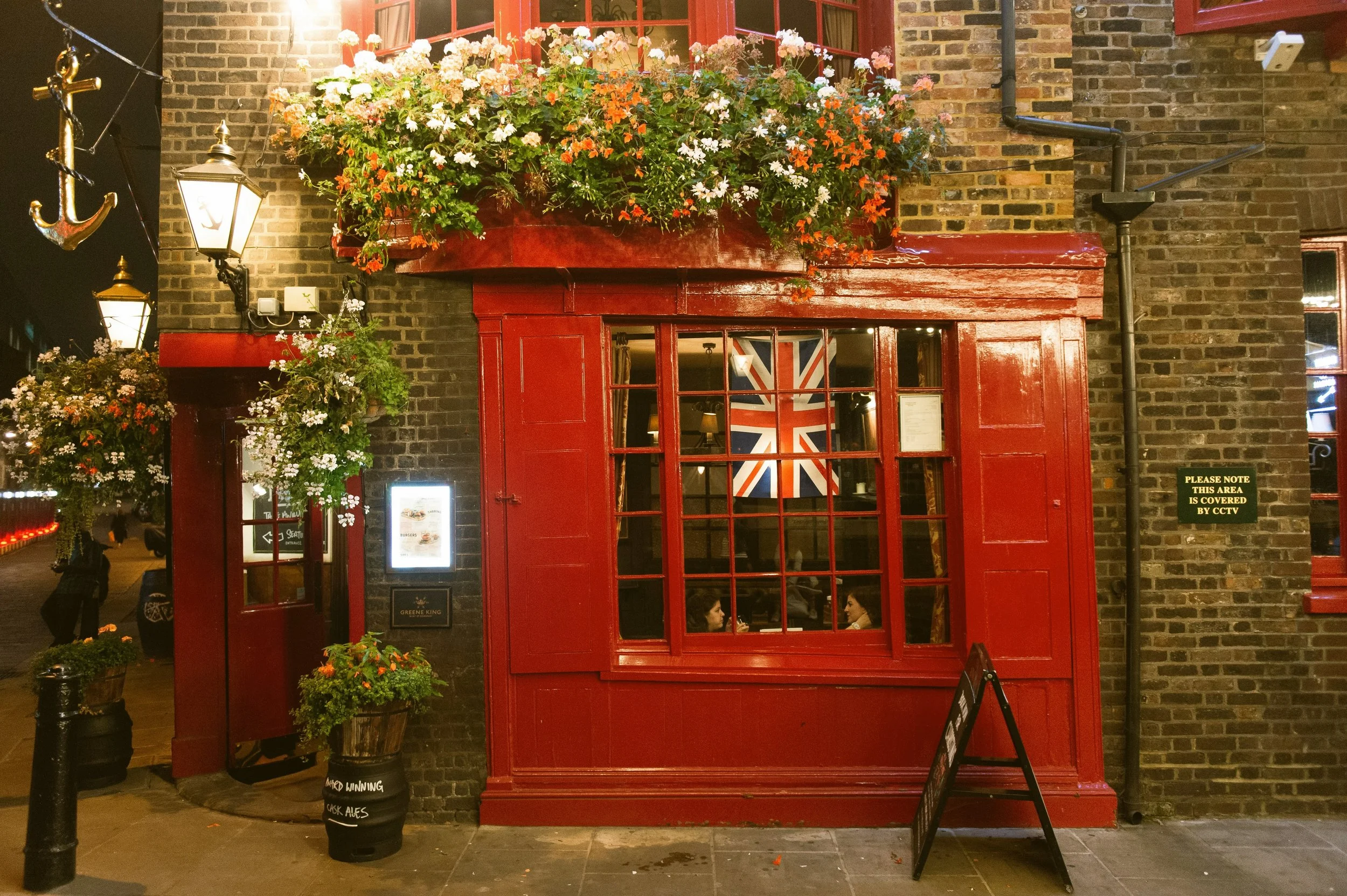 Red pub facade with a Union Jack in the window and hanging flower baskets, London