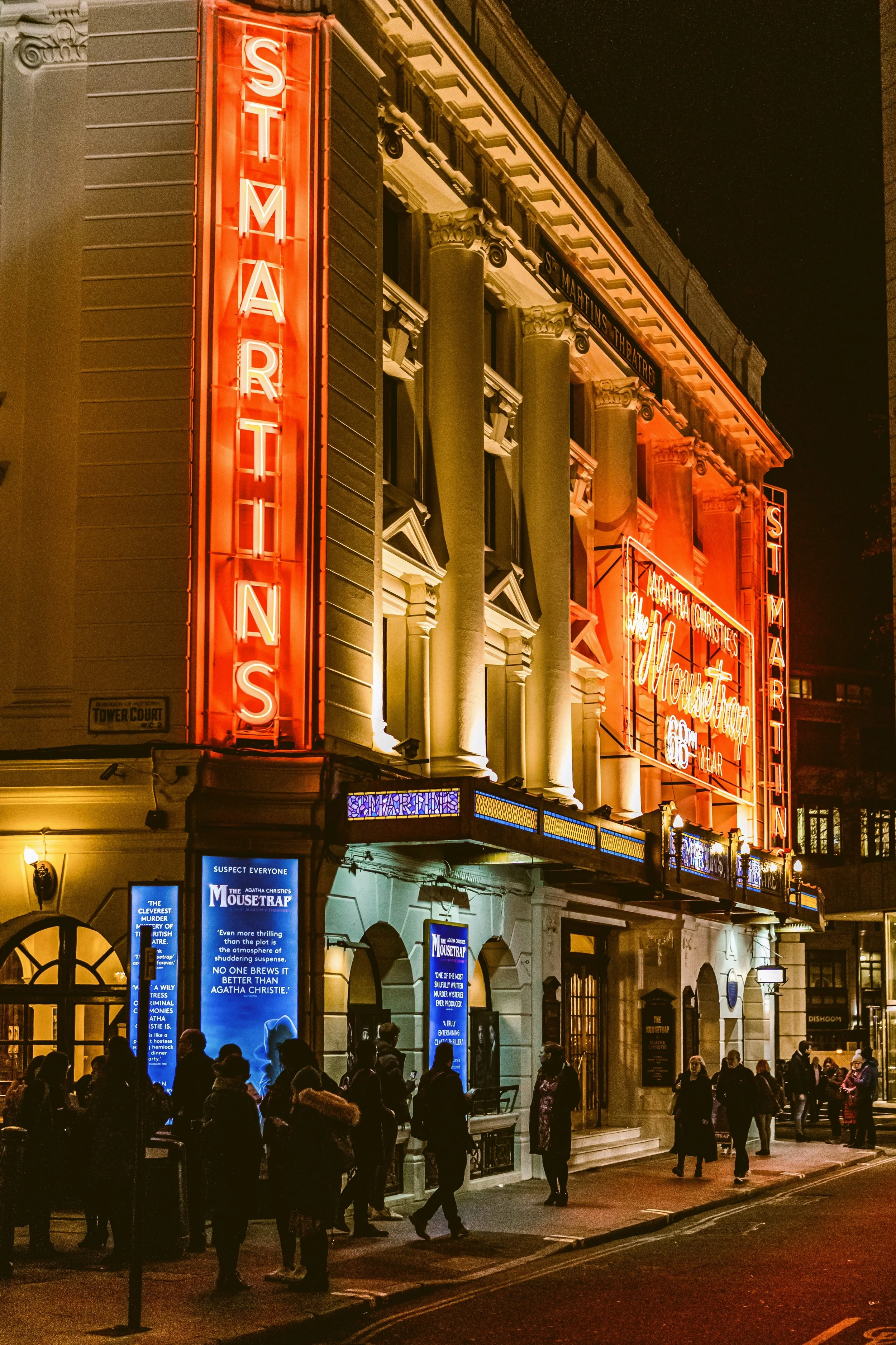 Red neon shopfronts lit up at night in the West End, London.