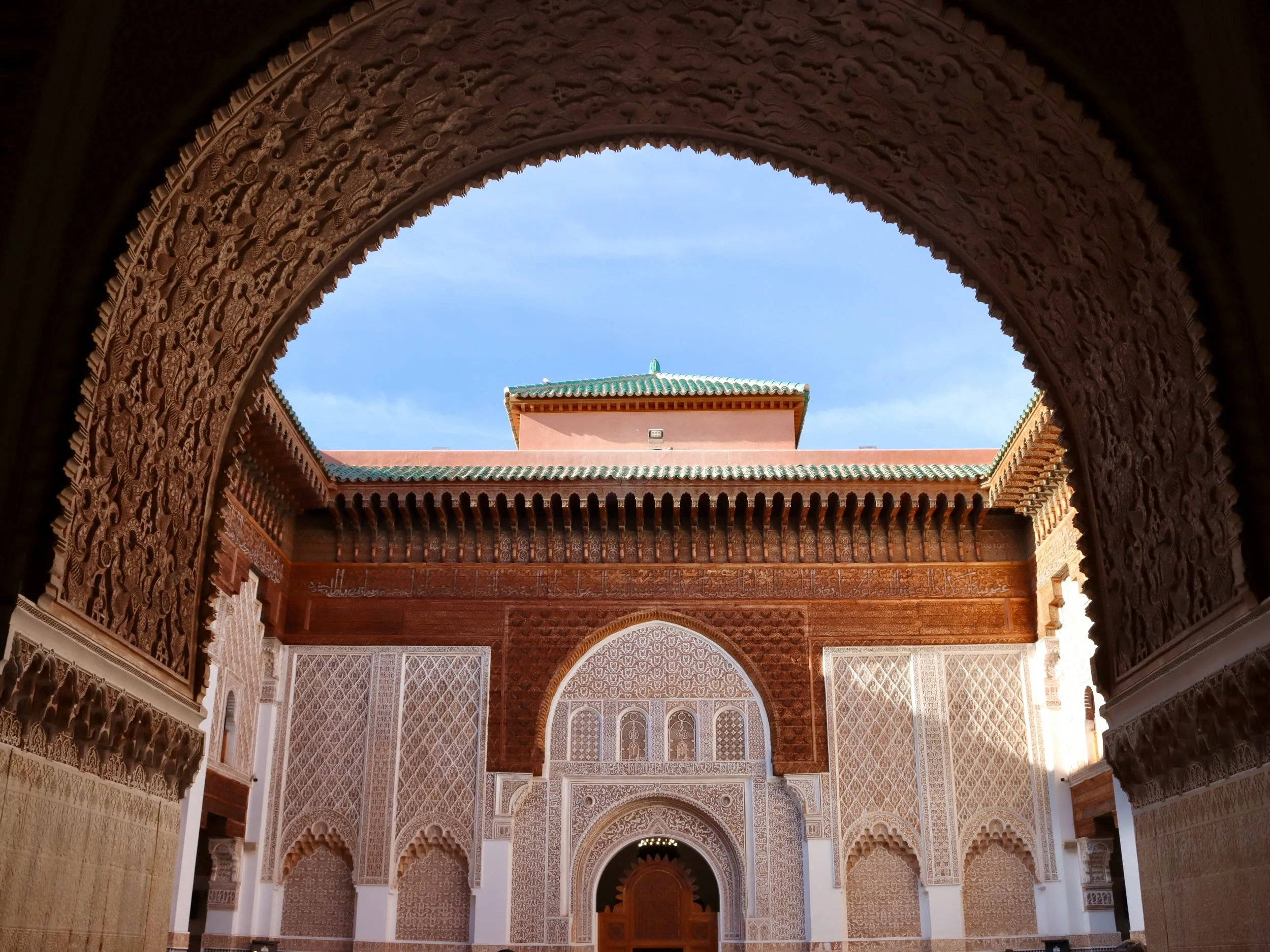 Ornate carved-cedar and stucco courtyard seen through a horseshoe arch, Ben Youssef Madrasa, Marrakech.
