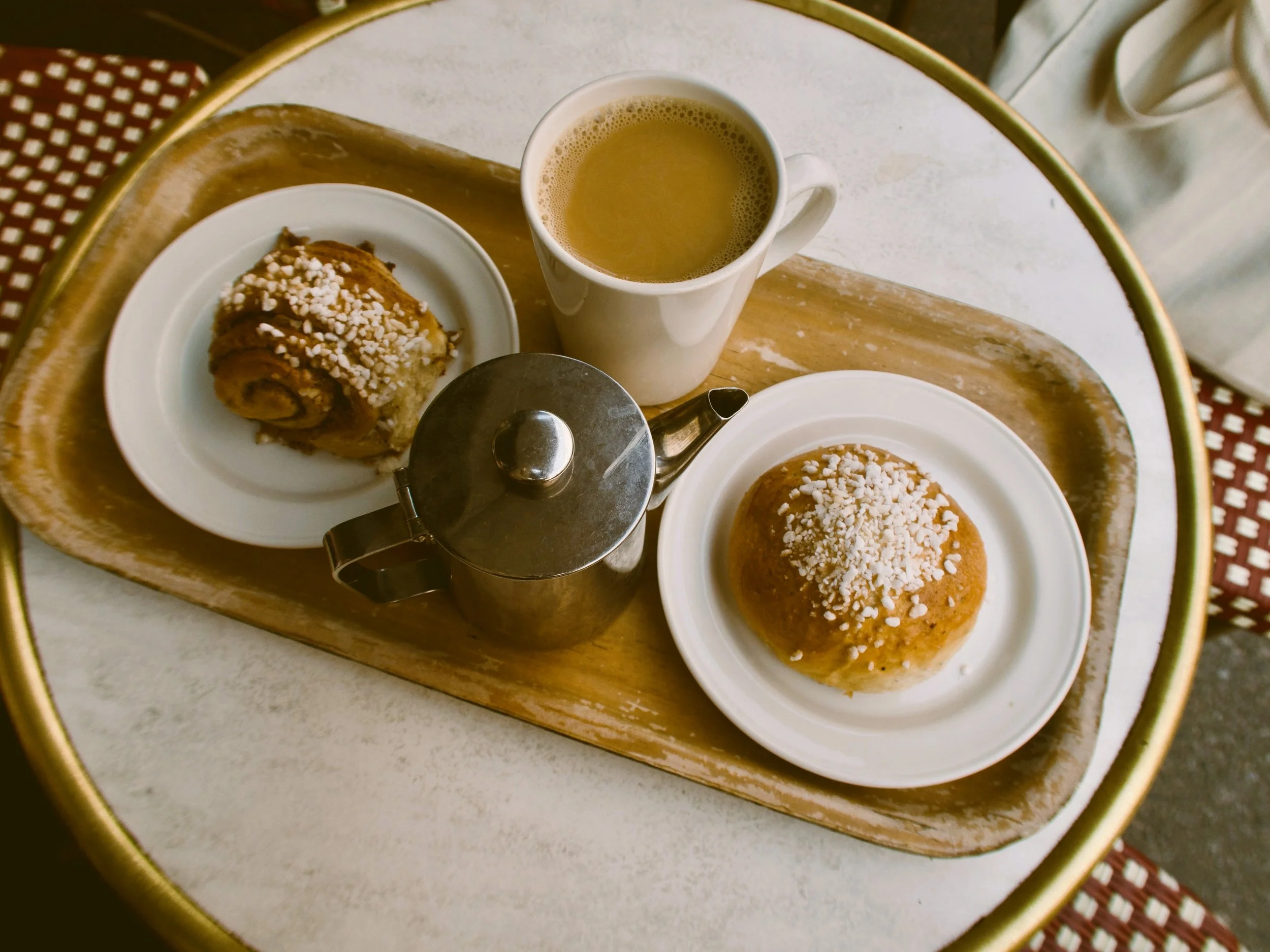 Fika, A tray with a cup of coffee two cinnamon rolls with white sprinkles on white plates, and a metal teapot.
