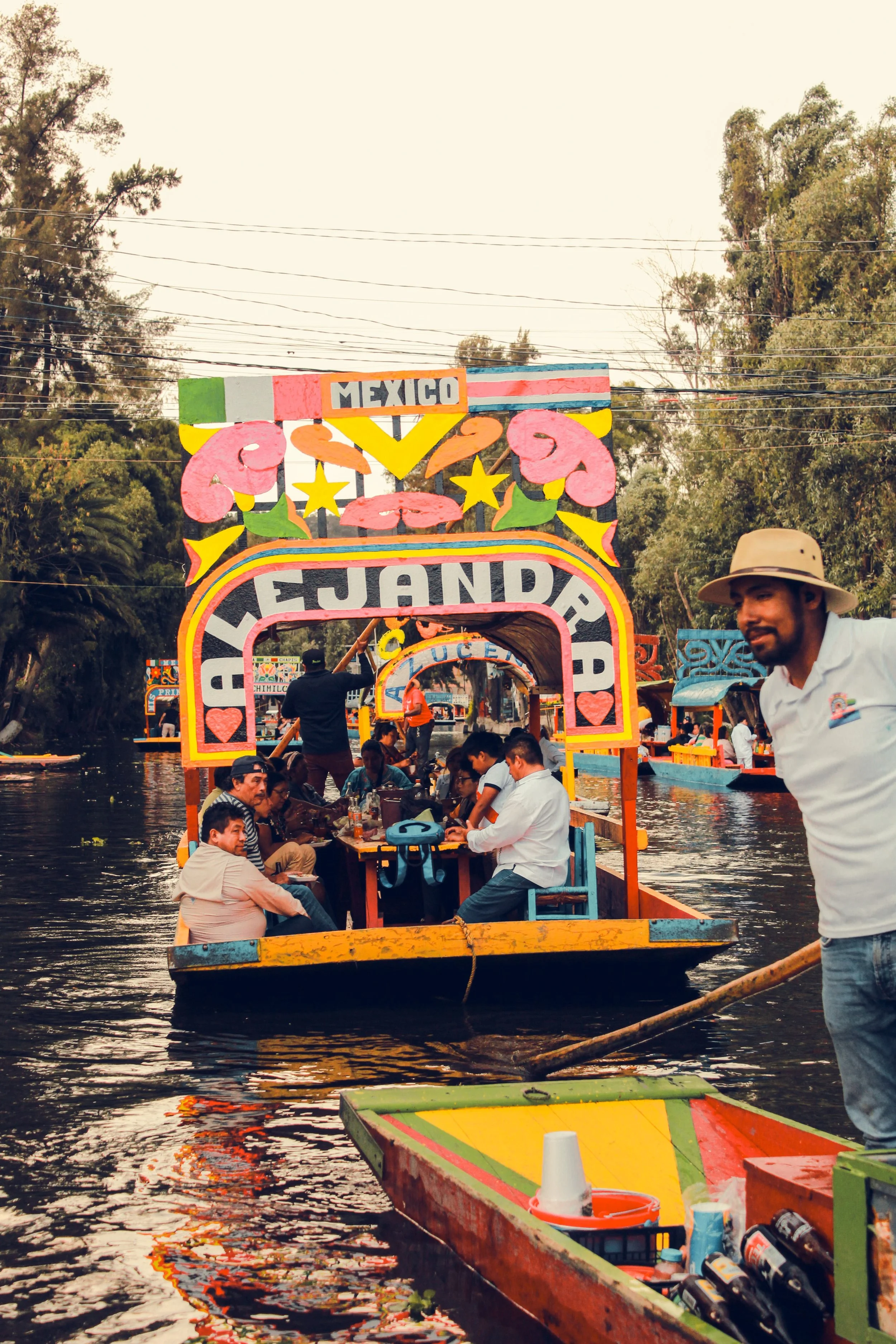 Colorful trajinera with a floral arch on a narrow canal with a boat vendor alongside, Xochimilco, Mexico City.