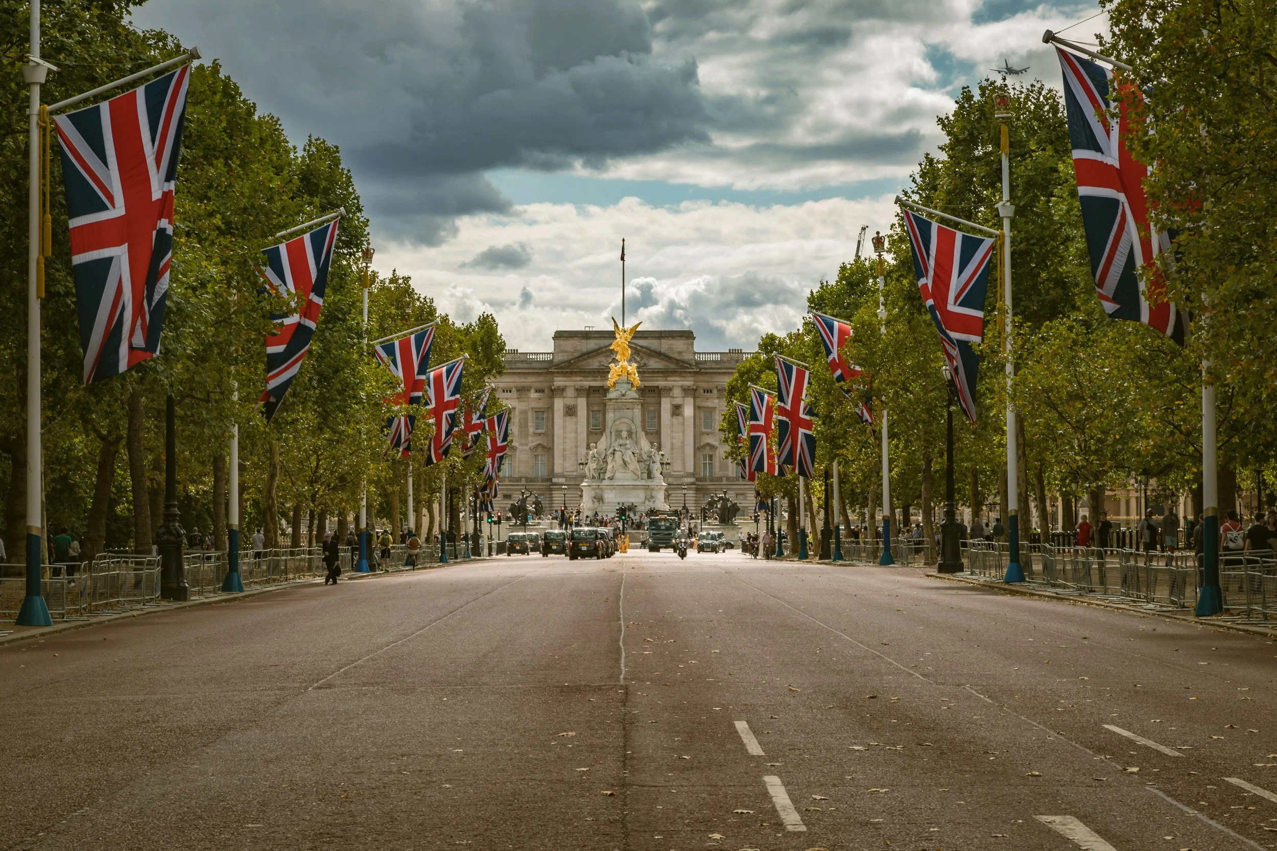 The Mall lined with Union Jack flags leading toward Buckingham Palace under a cloudy sky, London