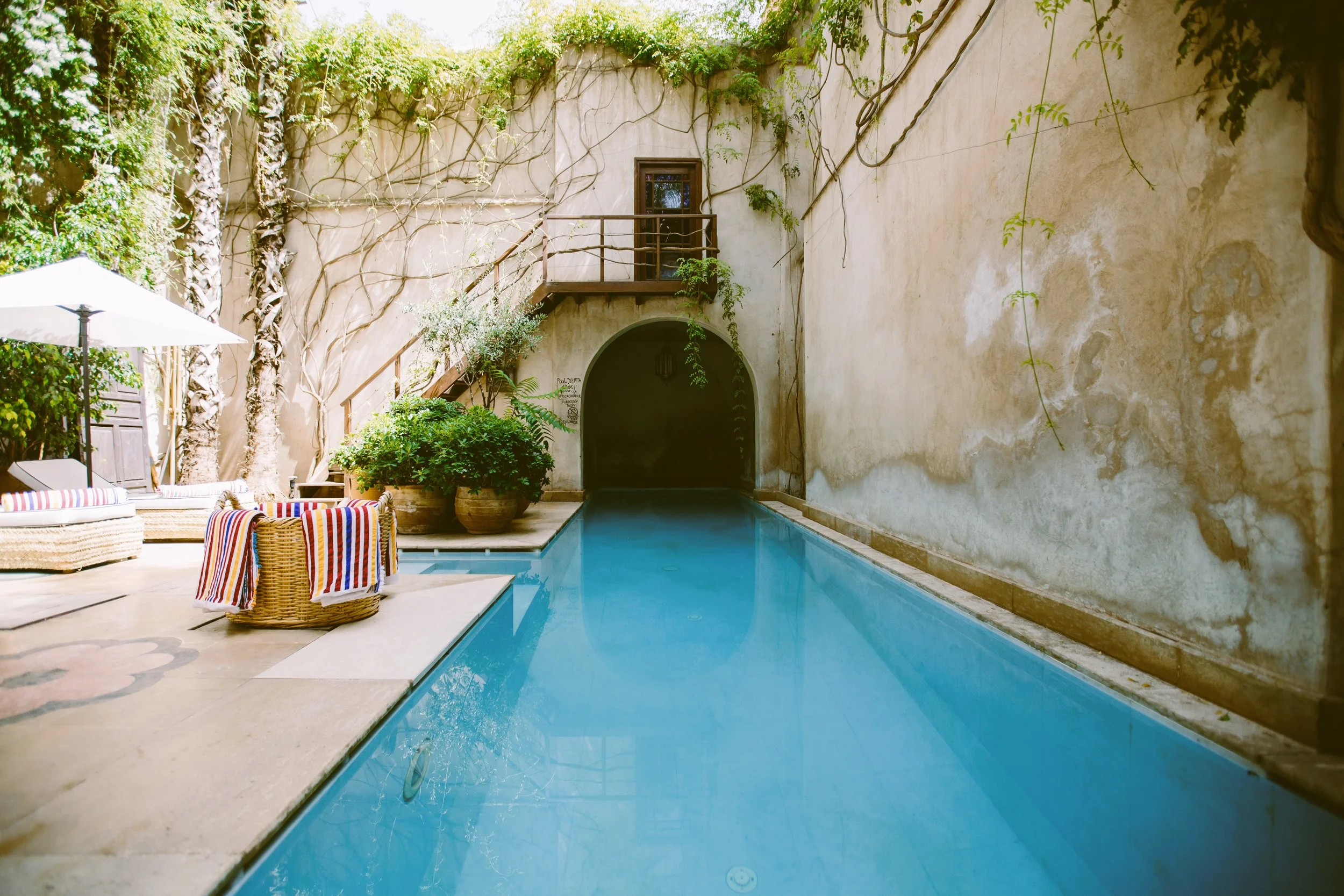 El Fenn courtyard pool with weathered ochre walls, climbing plants and a staircase, Marrakech.