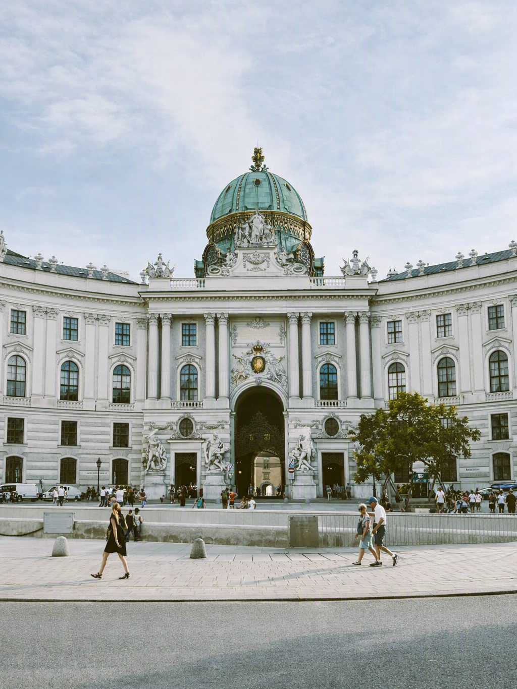 Hofburg Palace facade with its green dome and a cobblestone square in front, Vienna.