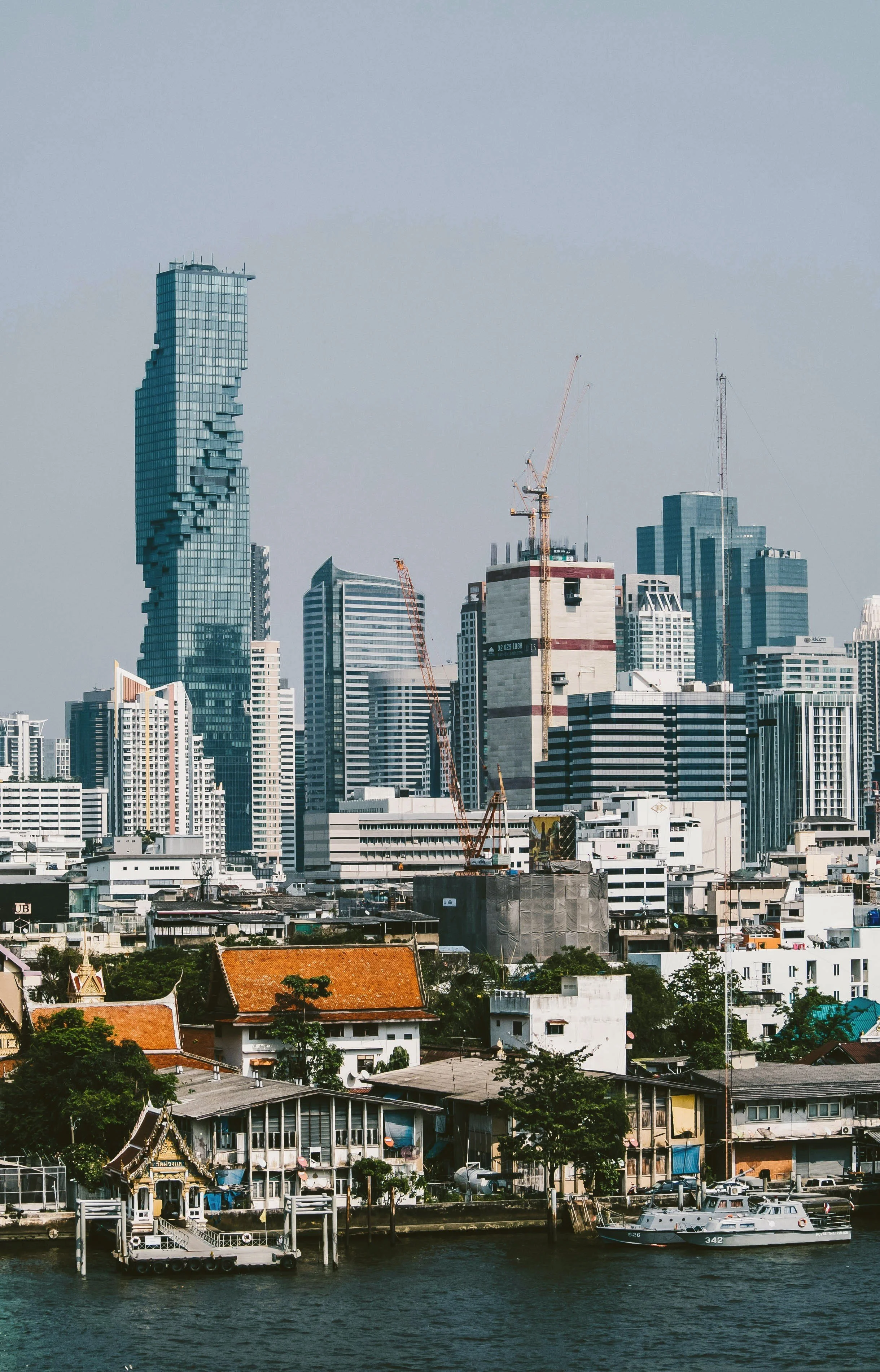 City skyline with glass towers rising above low-rise buildings along the river, Bangkok.