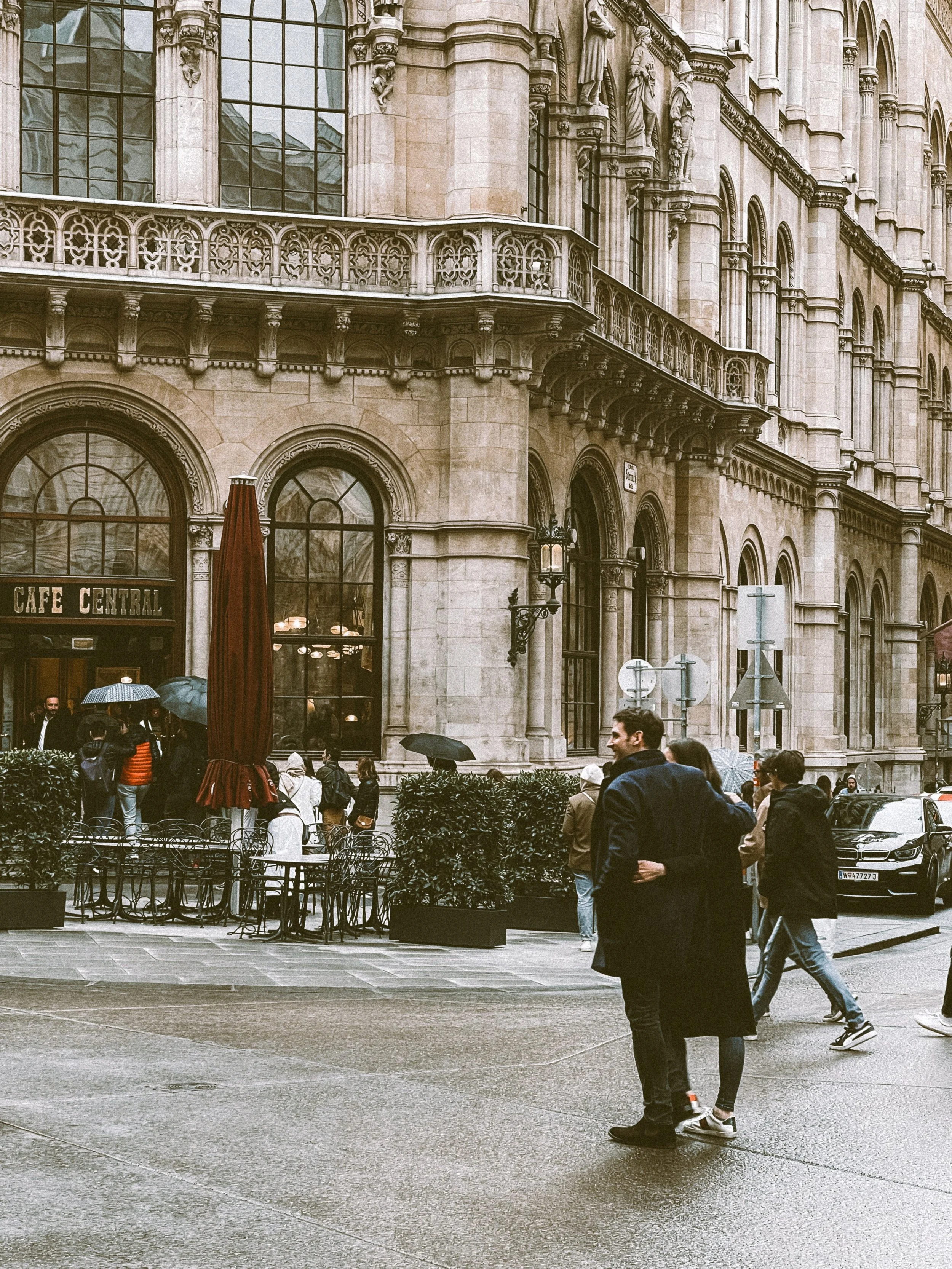 Café Central exterior with its ornate stone facade and arched windows, a person in a dark coat walking by, Vienna.