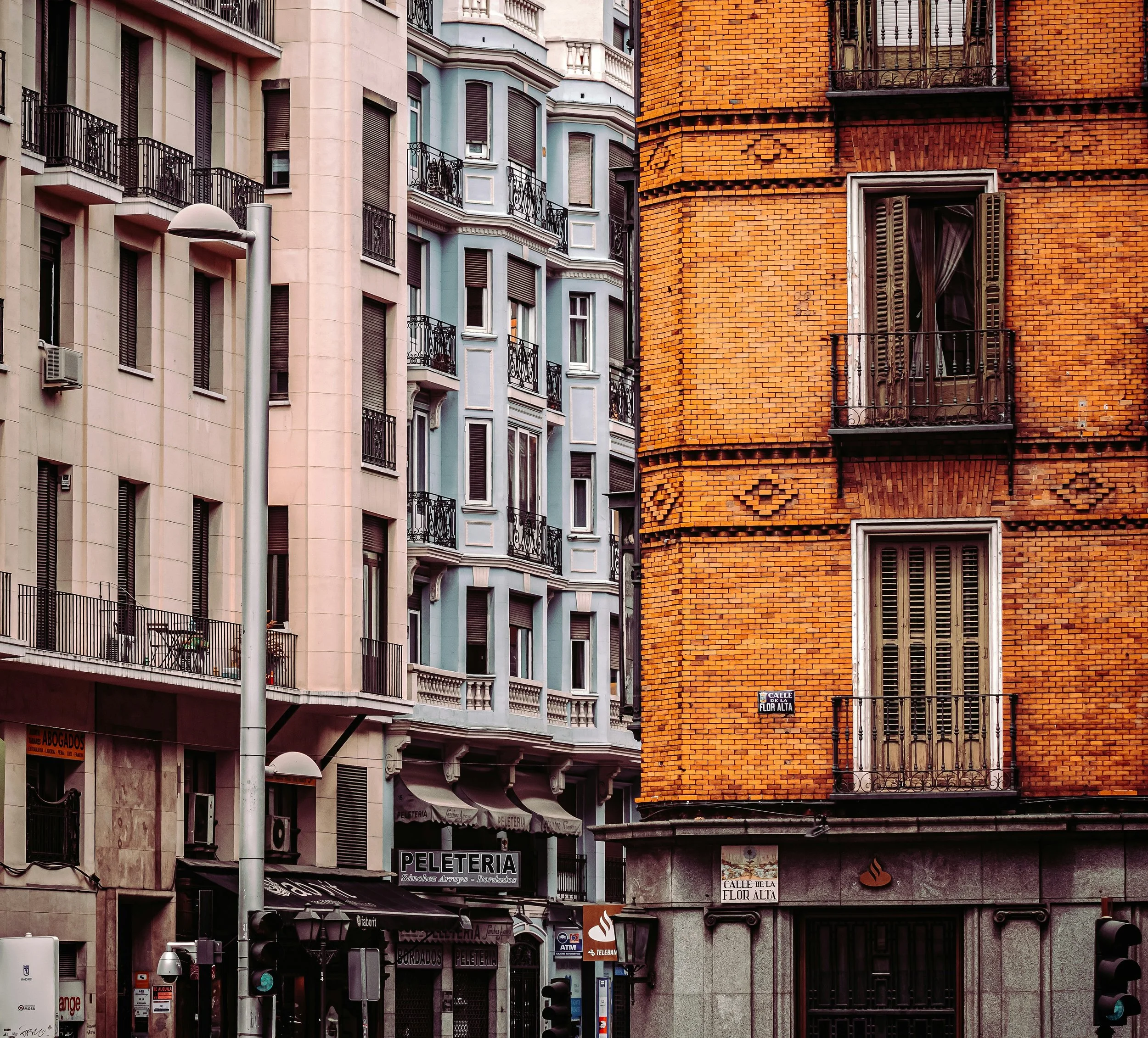 Orange brick corner building with shuttered windows beside pastel townhouses on a city street, Madrid