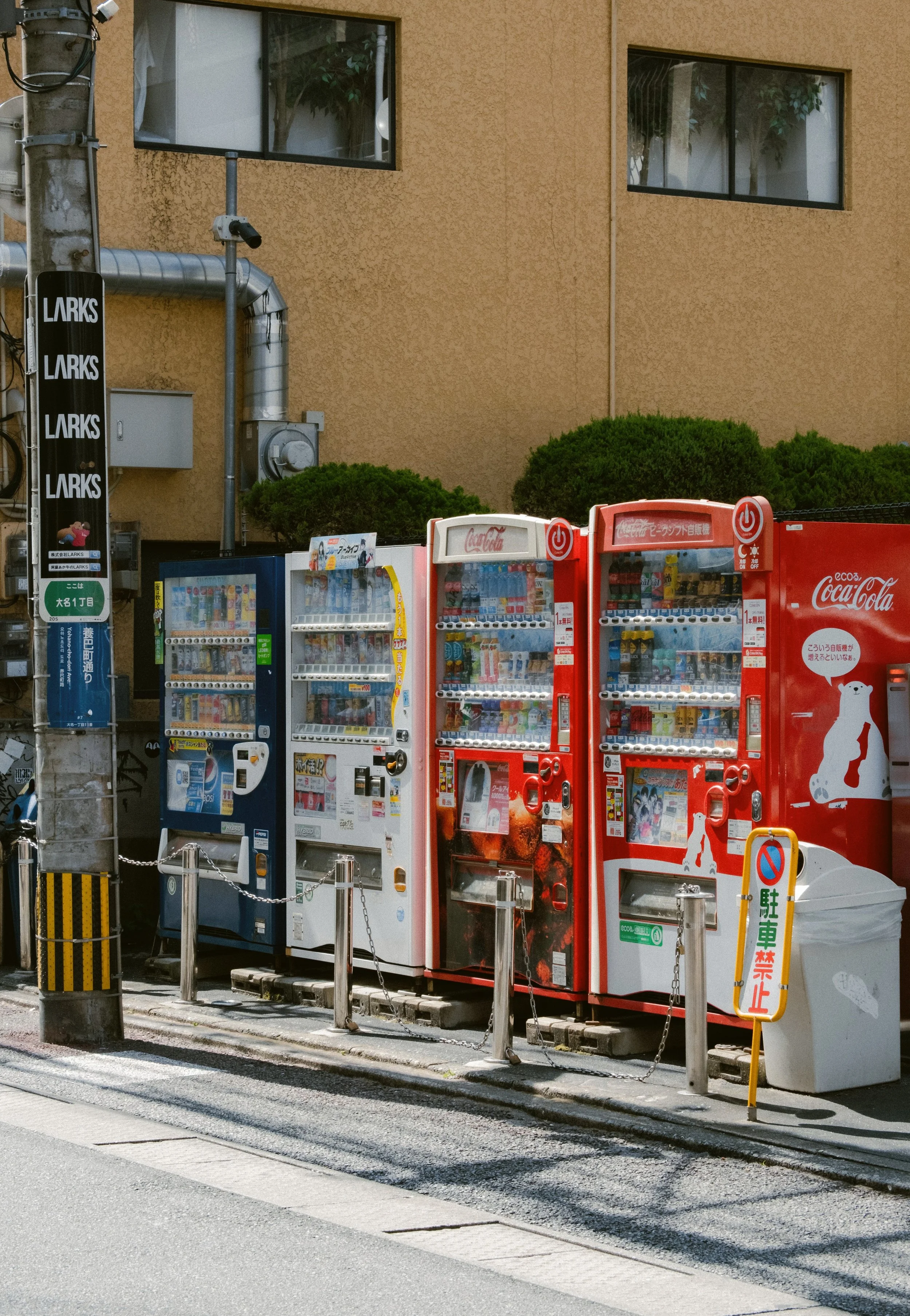 Row of red and white vending machines on a street corner beside a brick building, Tokyo.