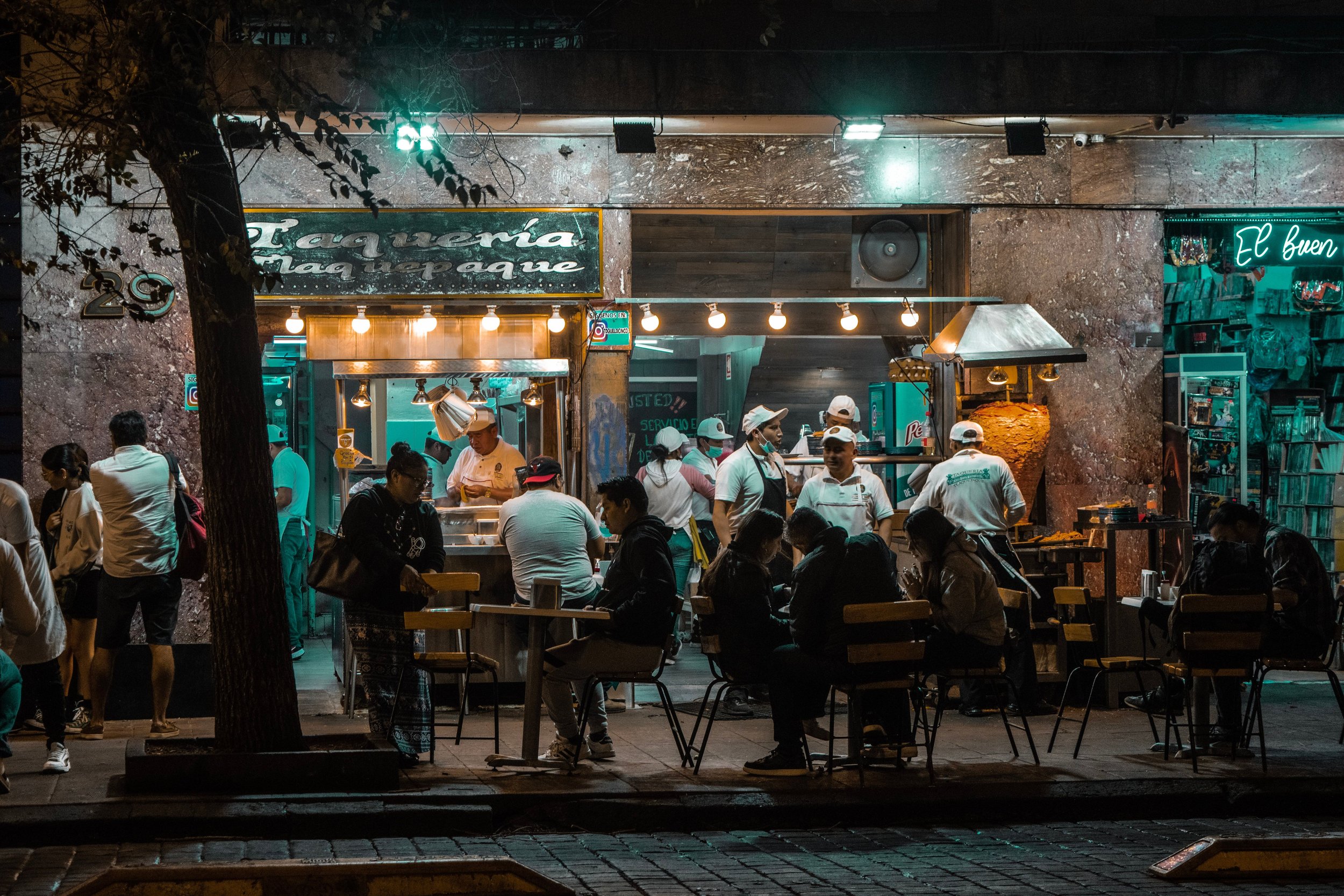 Taco stand lit up at night with people gathered around the counter under warm lights, Mexico City.