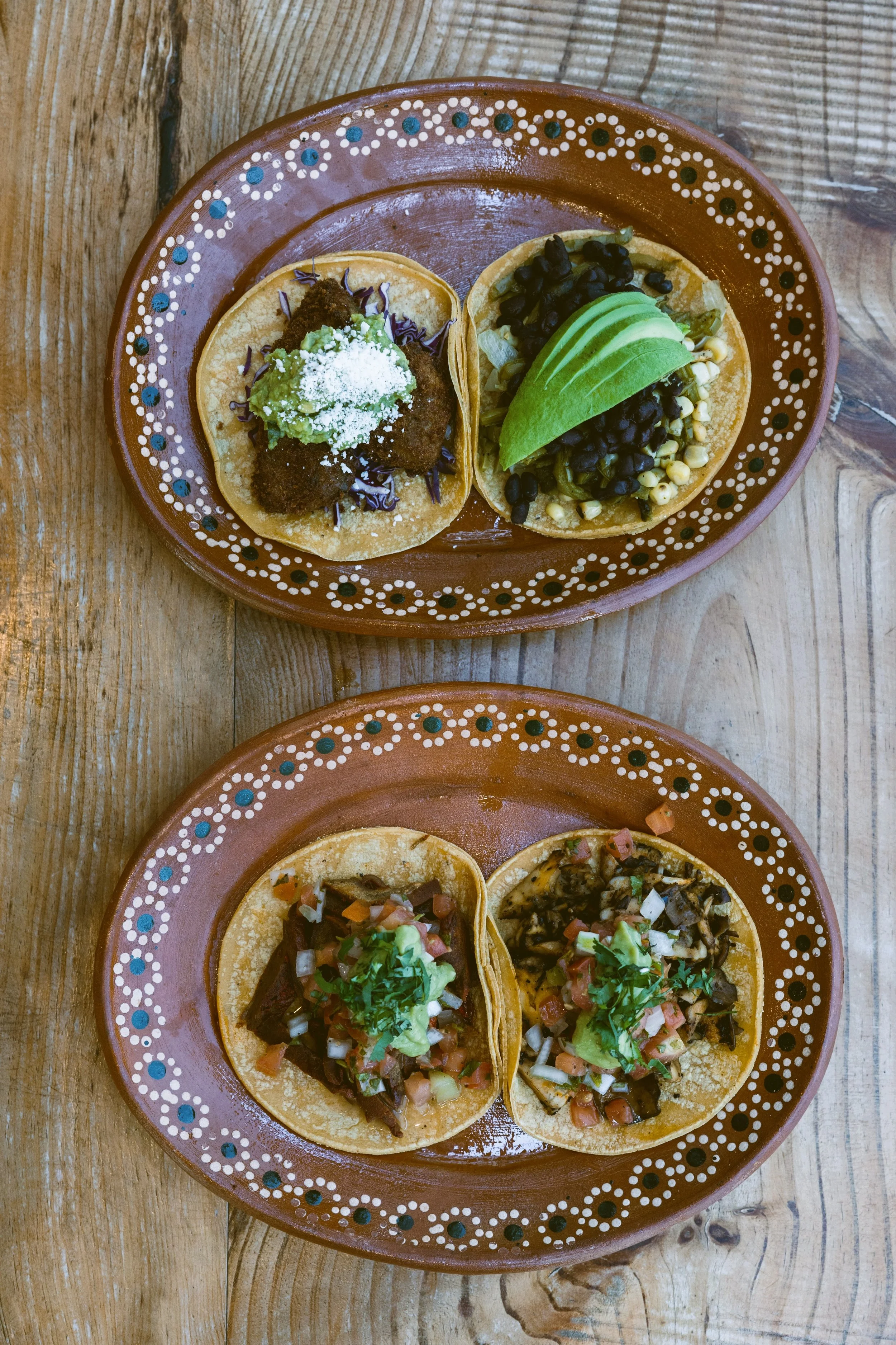 Overhead view of tacos served on two decorated ceramic plates on a wooden table, Mexico City.