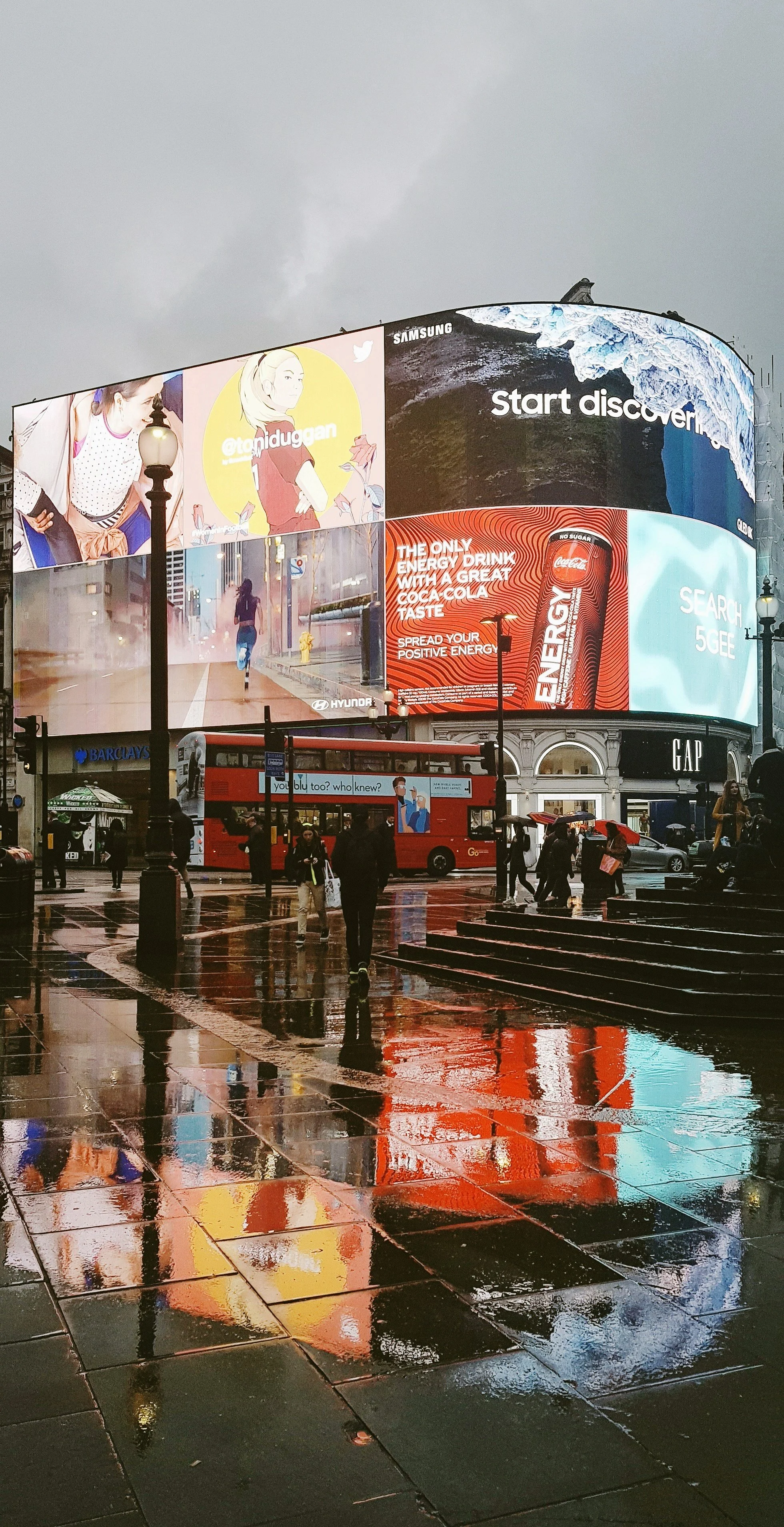 Illuminated billboards reflected in wet pavement at Piccadilly Circus, London
