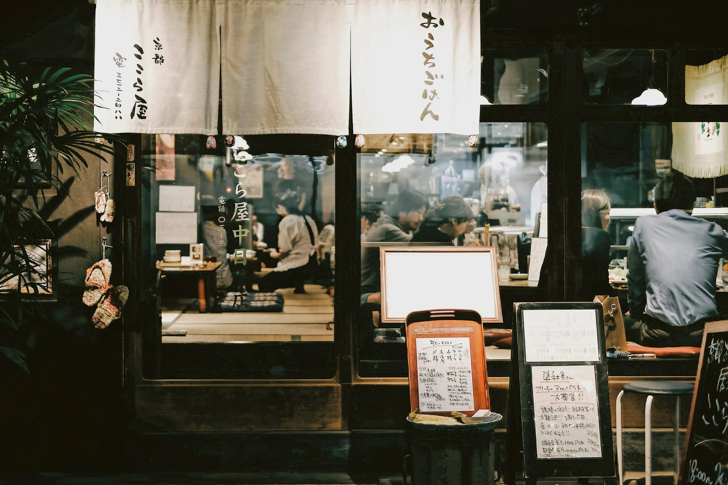 Traditional Japanese restaurant with noren curtains at the entrance and diners seated inside at night, Tokyo