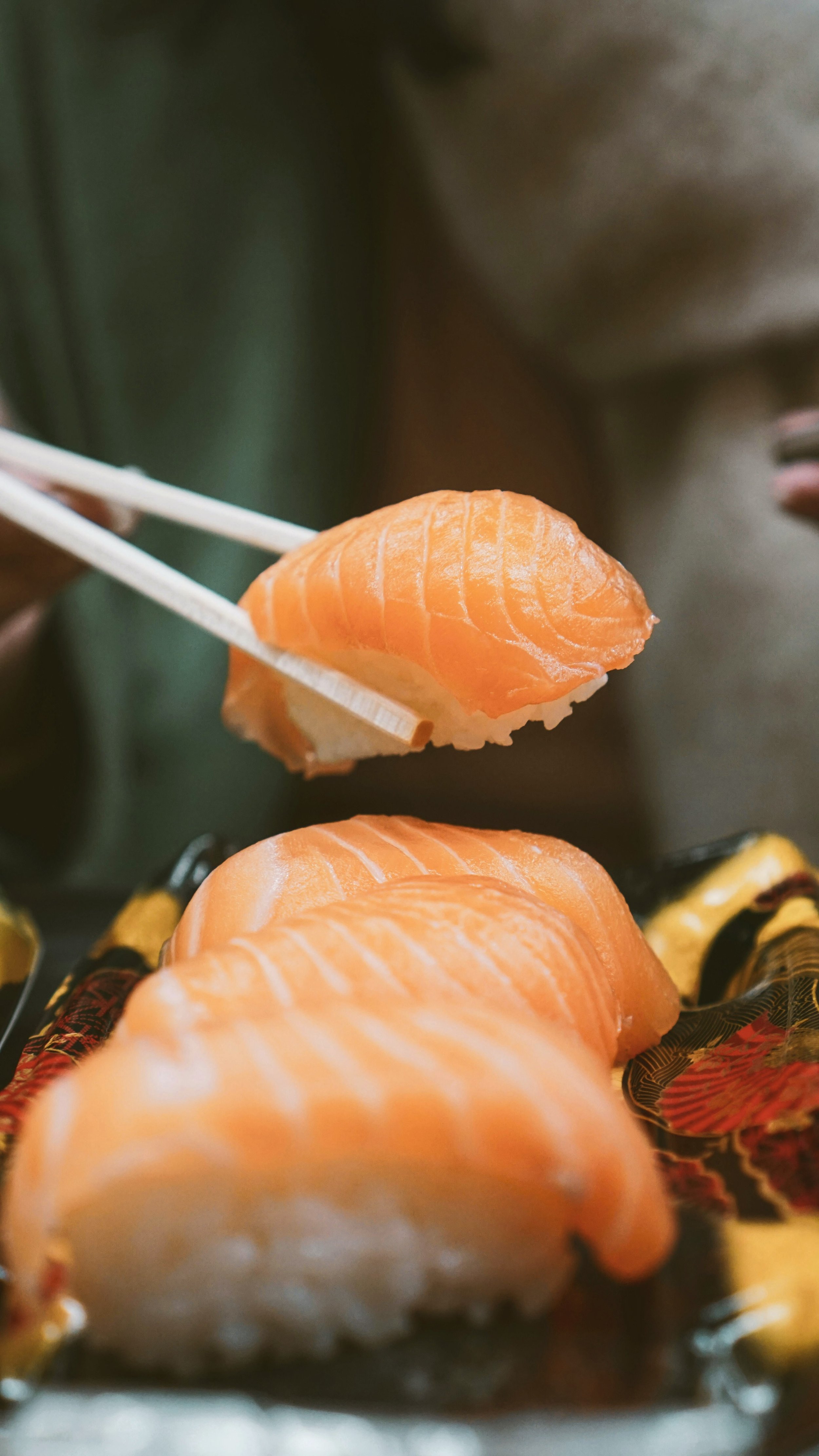 Chopsticks lifting a piece of salmon nigiri from a plate of sushi, Tokyo.