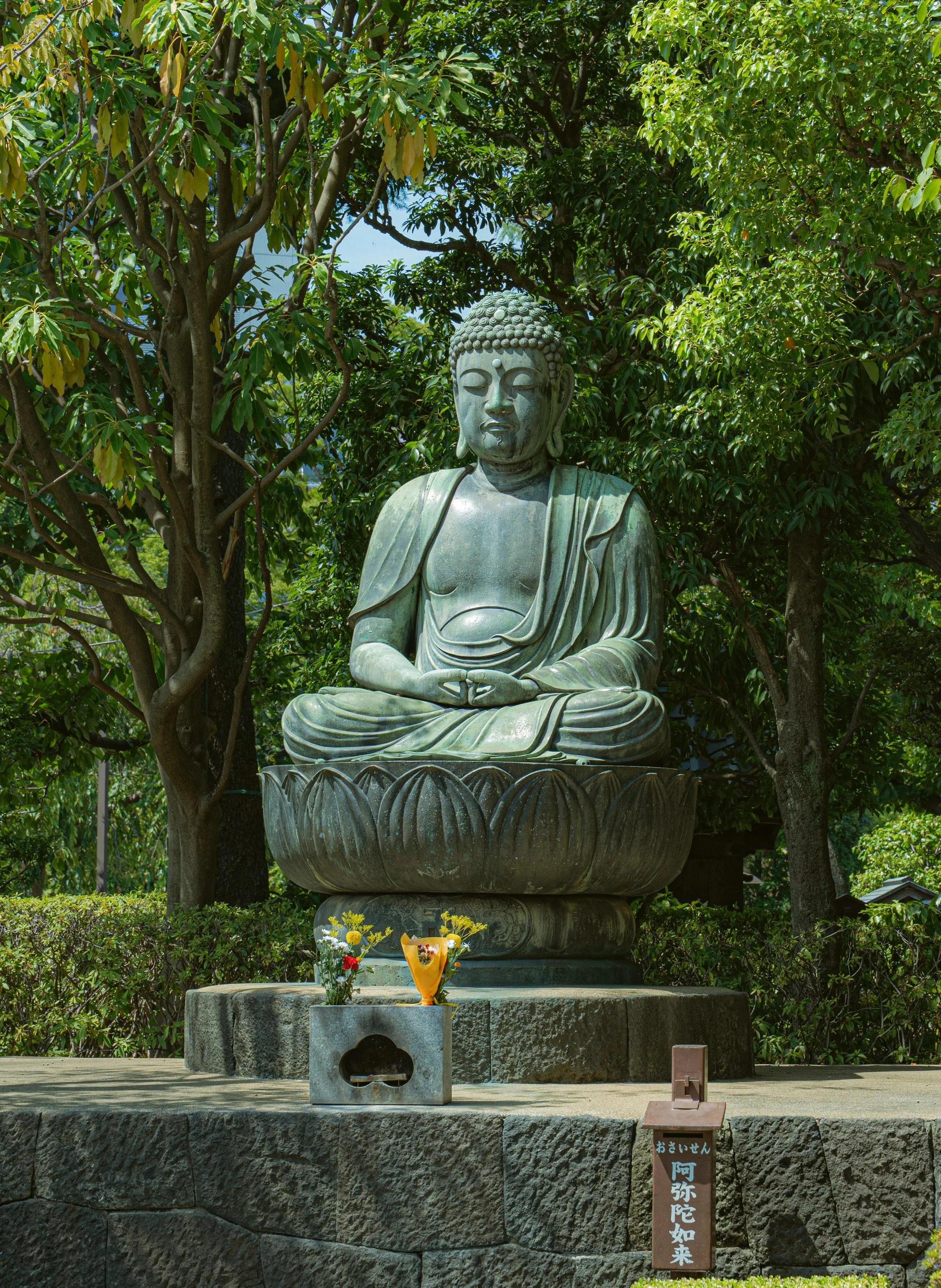 Bronze Buddha statue seated on a lotus pedestal among green trees, Tokyo