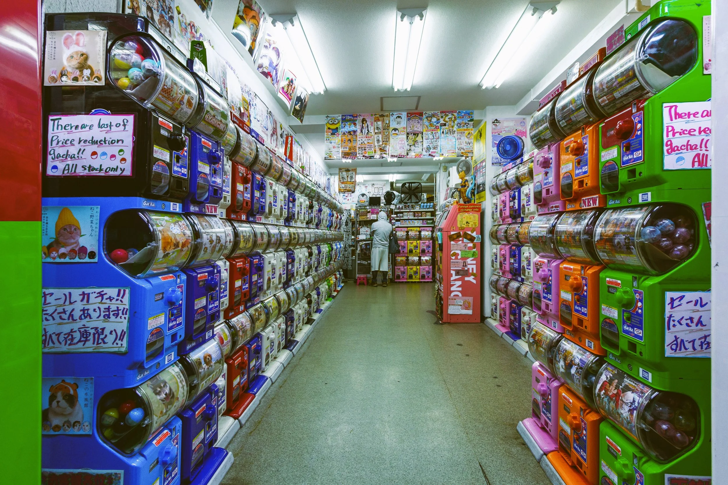 Narrow aisle lined with colorful gachapon capsule toy machines under bright lights, Tokyo.