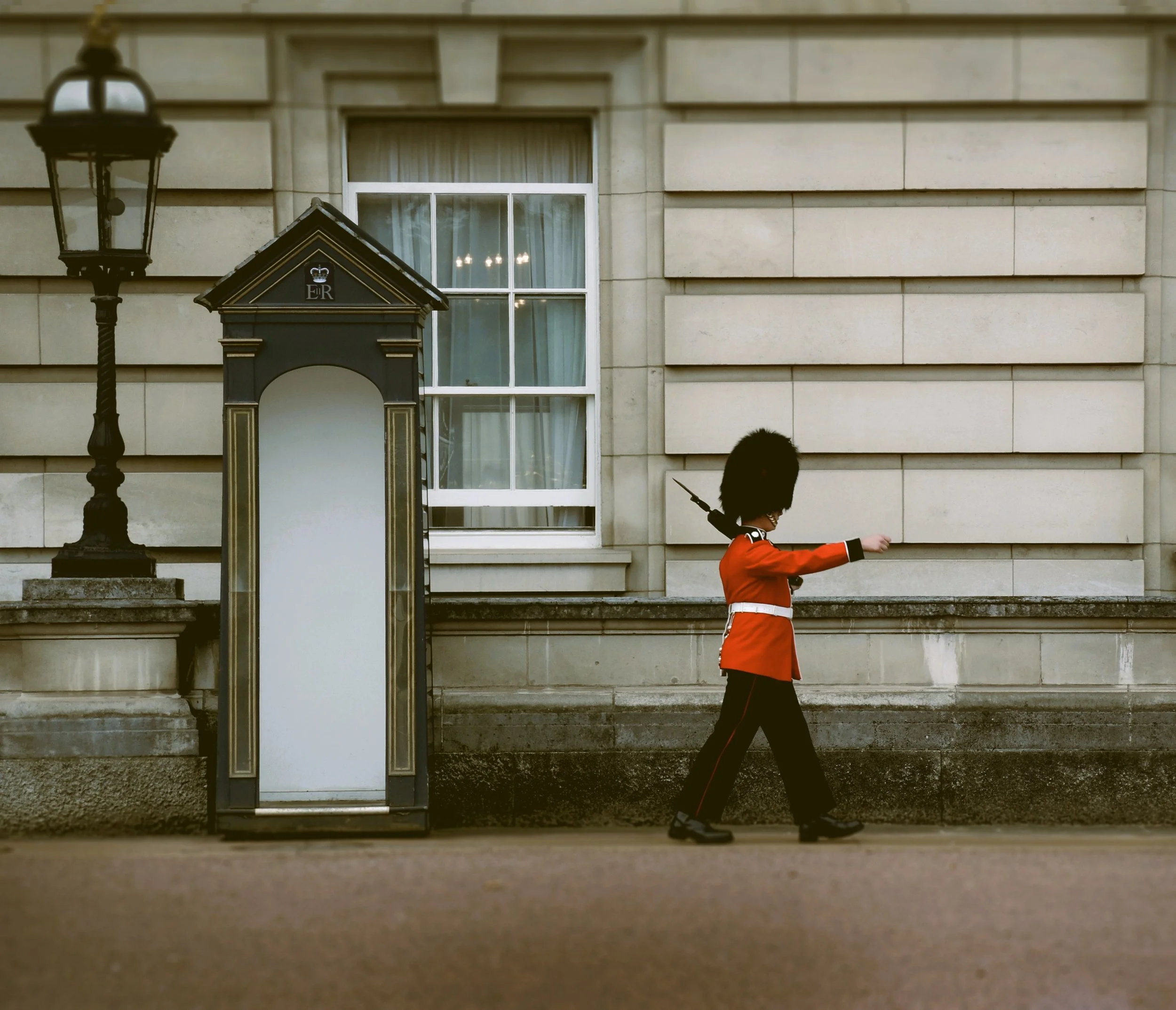 Royal guard in a red tunic walking past a sentry box outside Buckingham Palace, London