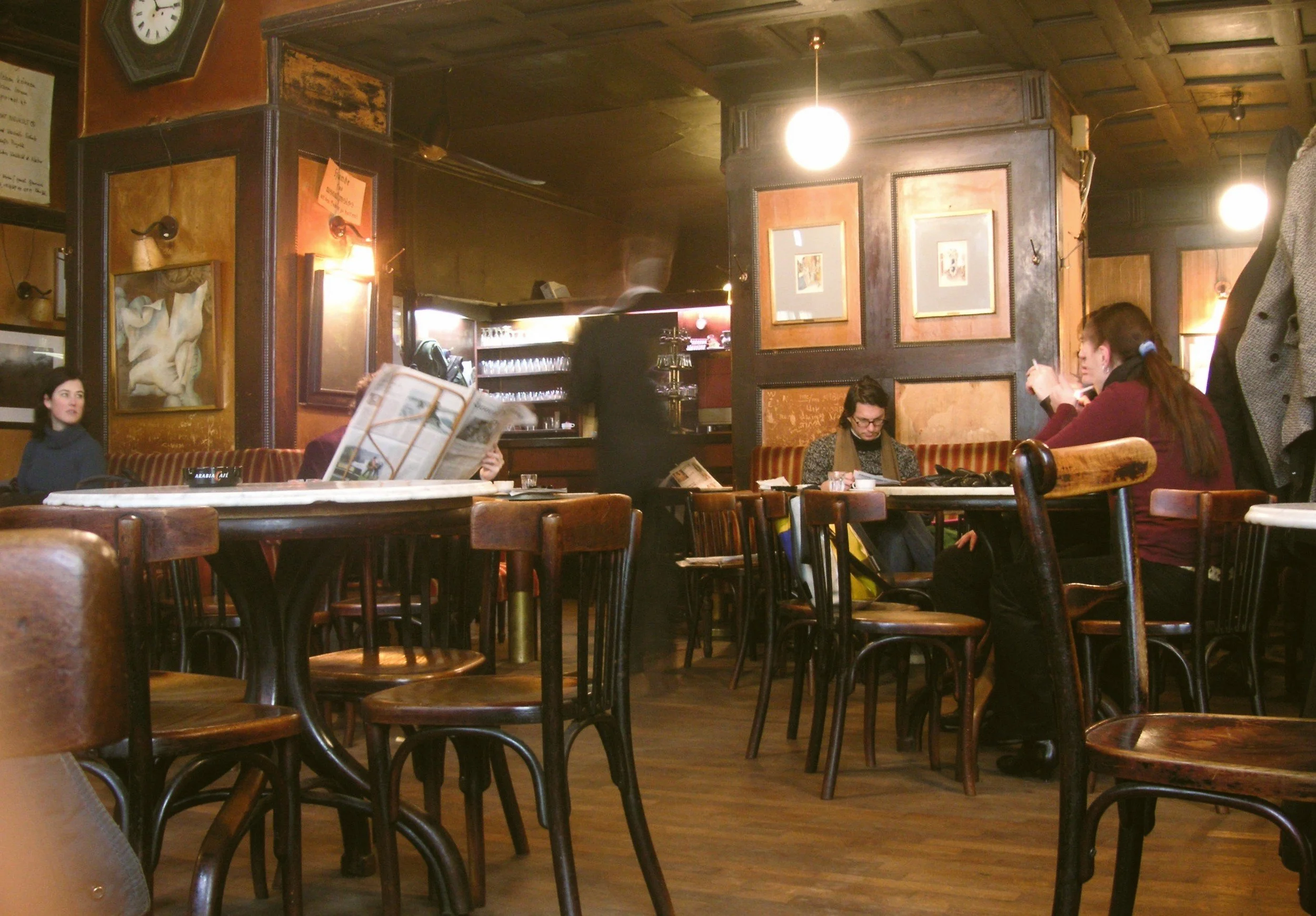 Café Hawelka interior with dark wood paneling, framed pictures on the walls and guests seated at small tables, Vienna.