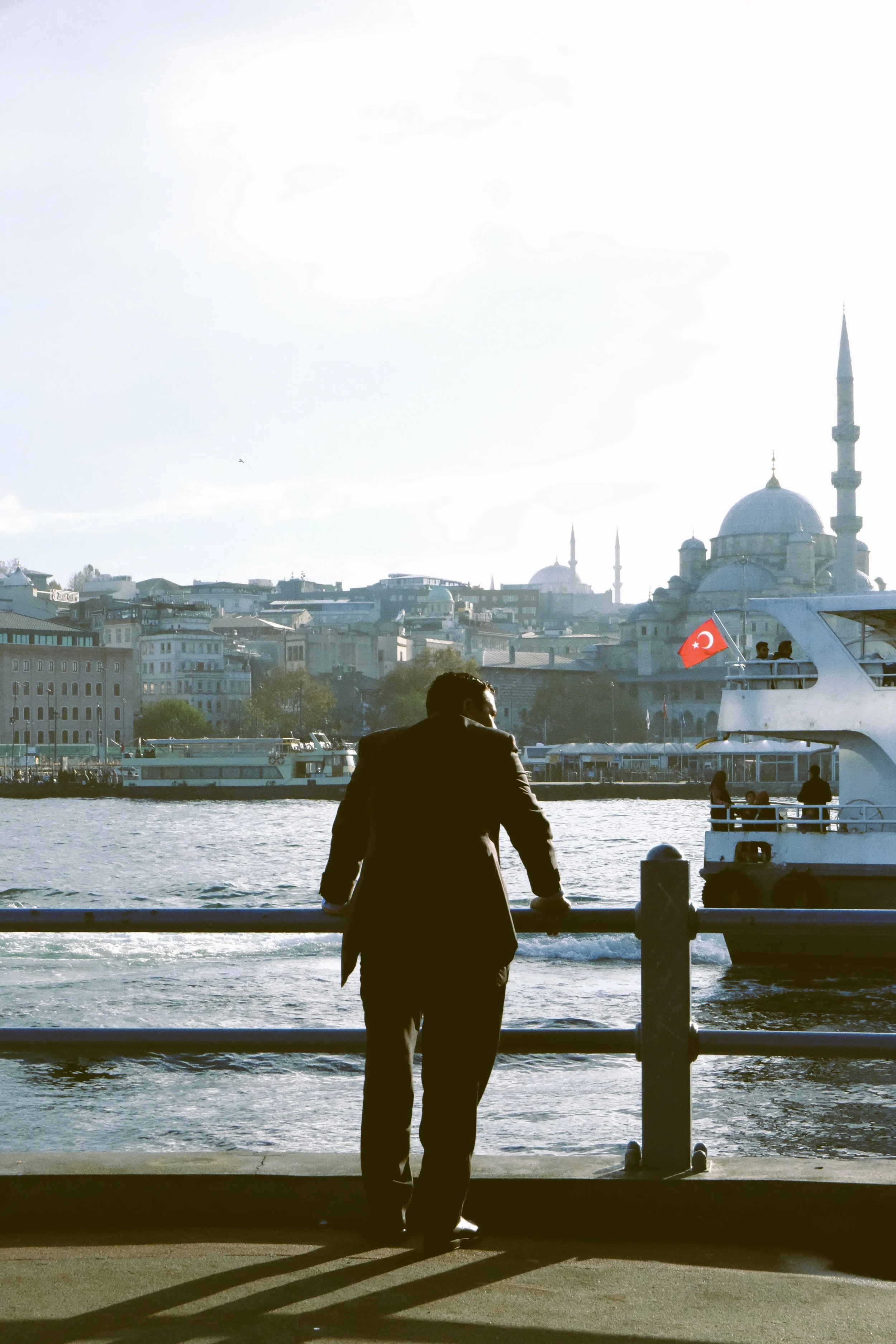 Person standing at a waterfront railing with a mosque skyline across the water, Istanbul.