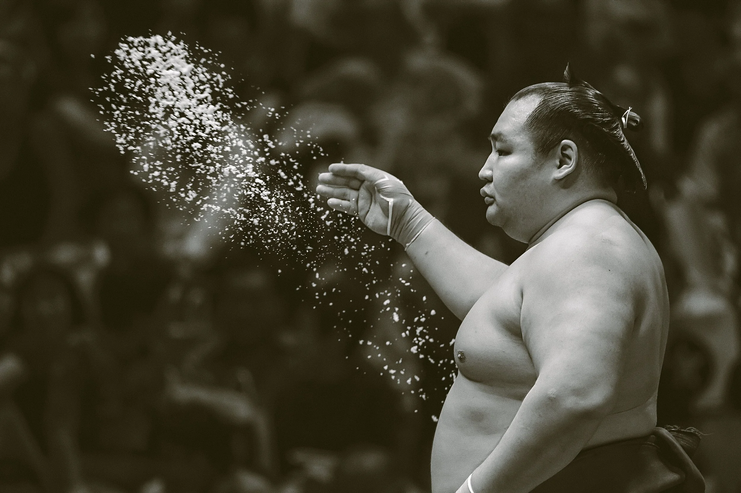 A sumo wrestler is tossing an unspecified amount of salt into the air before a sumo fight.
