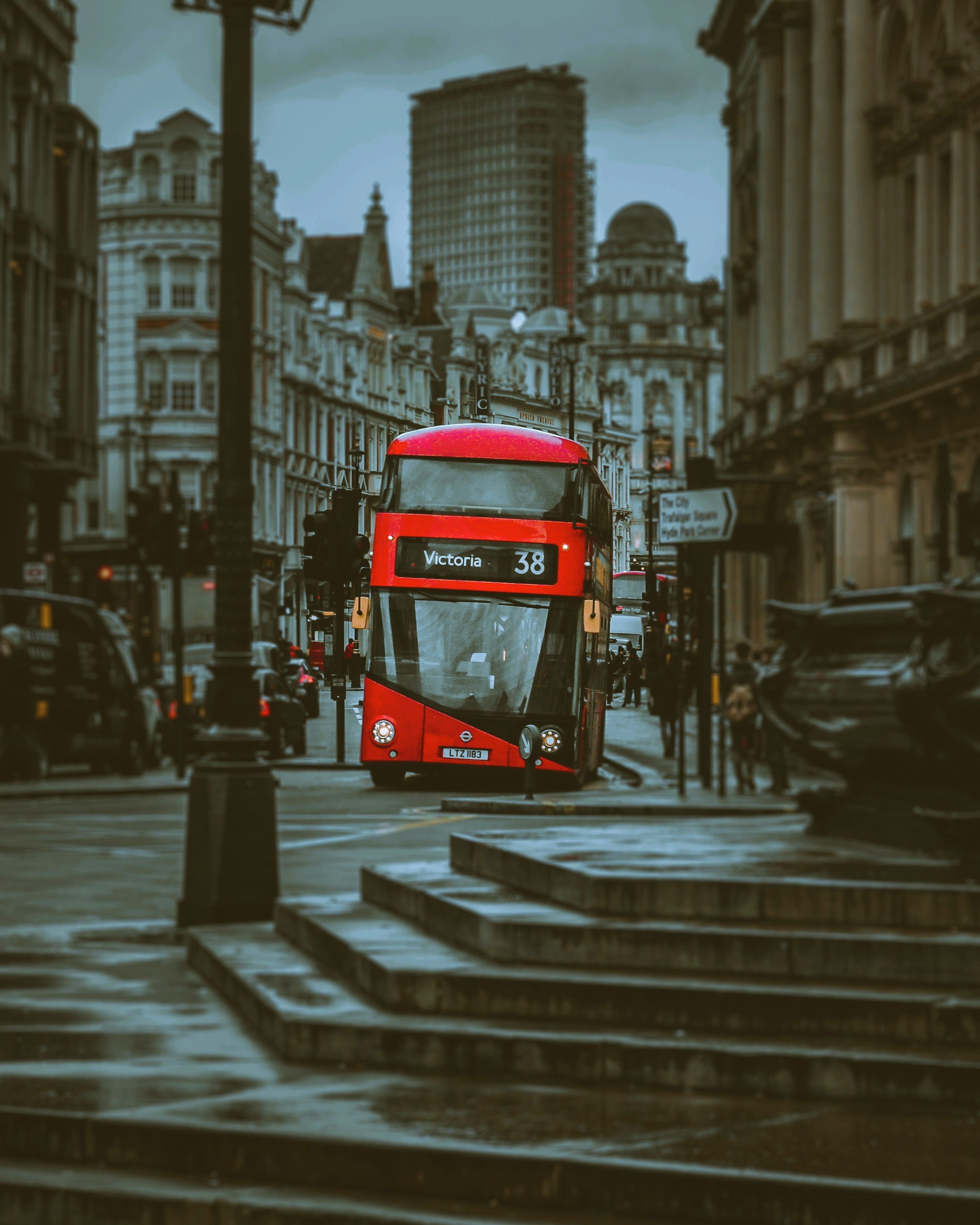 Red double-decker bus on a wet city street with skyscrapers behind, London