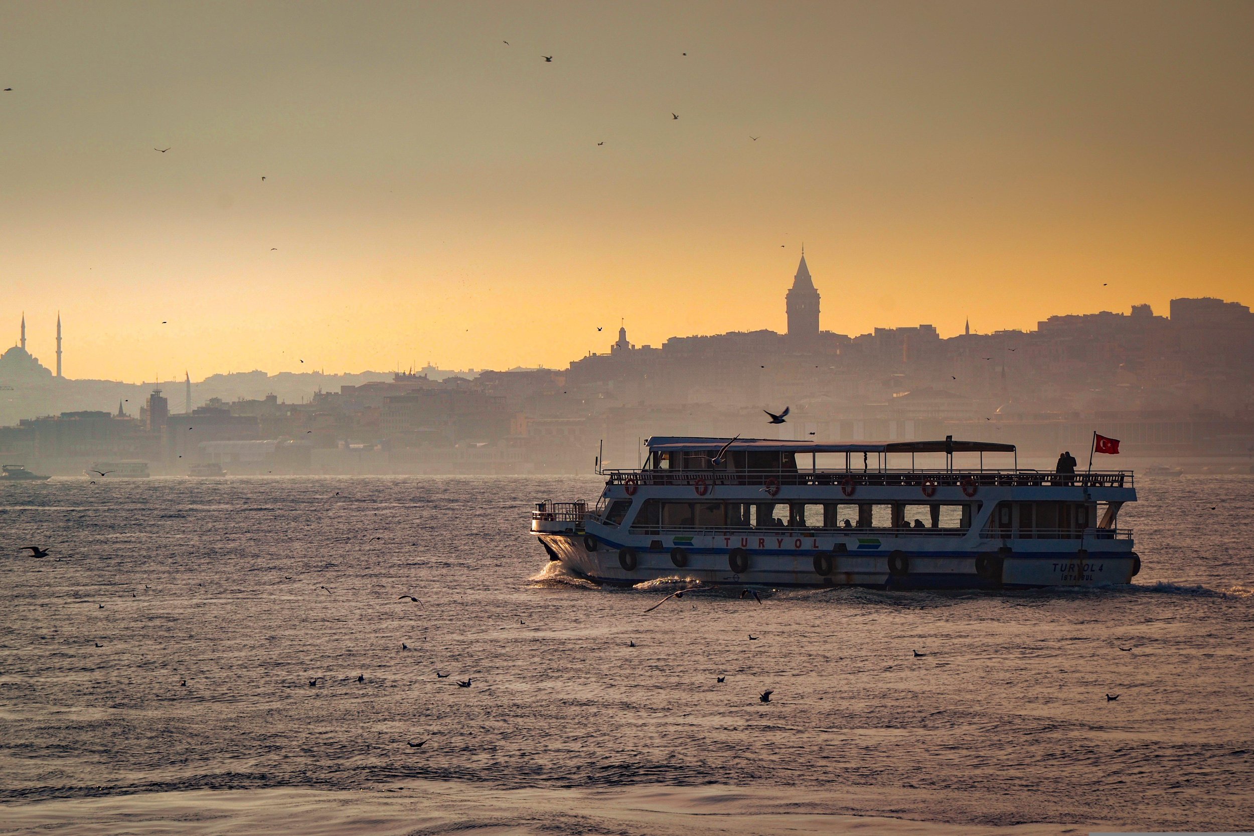 Ferry crossing the Bosphorus at sunset with the Istanbul skyline and Galata Tower in the distance.