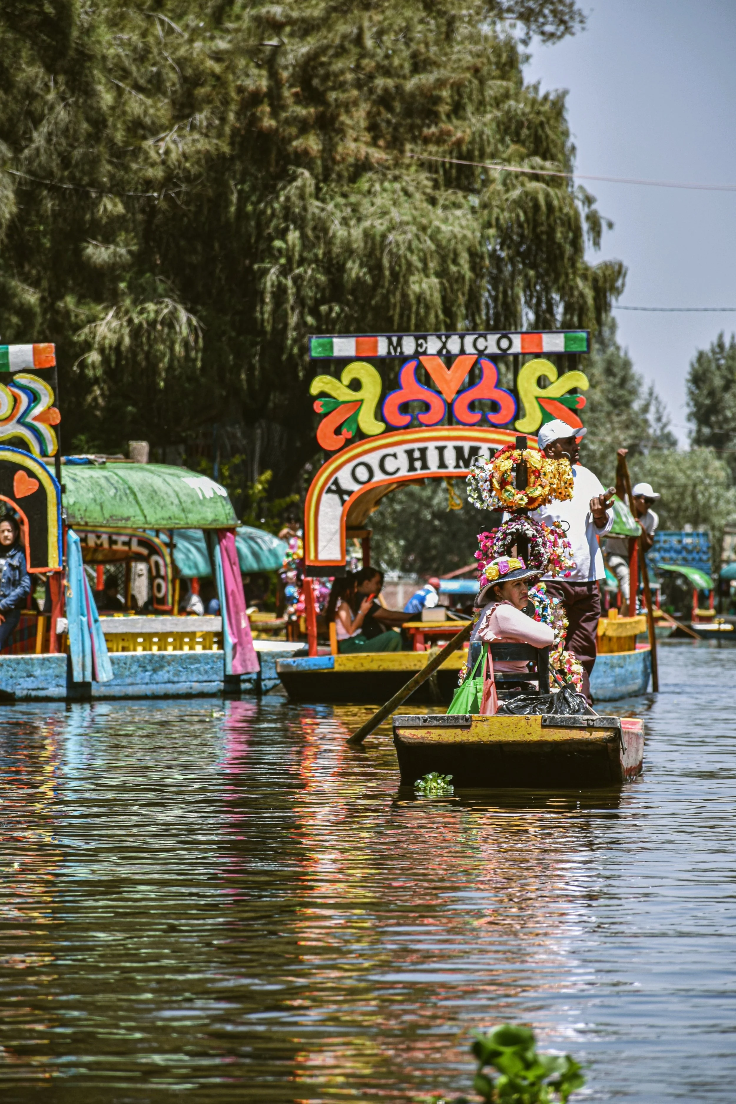 Colorful trajineras floating on a canal surrounded by trees, Xochimilco, Mexico City.