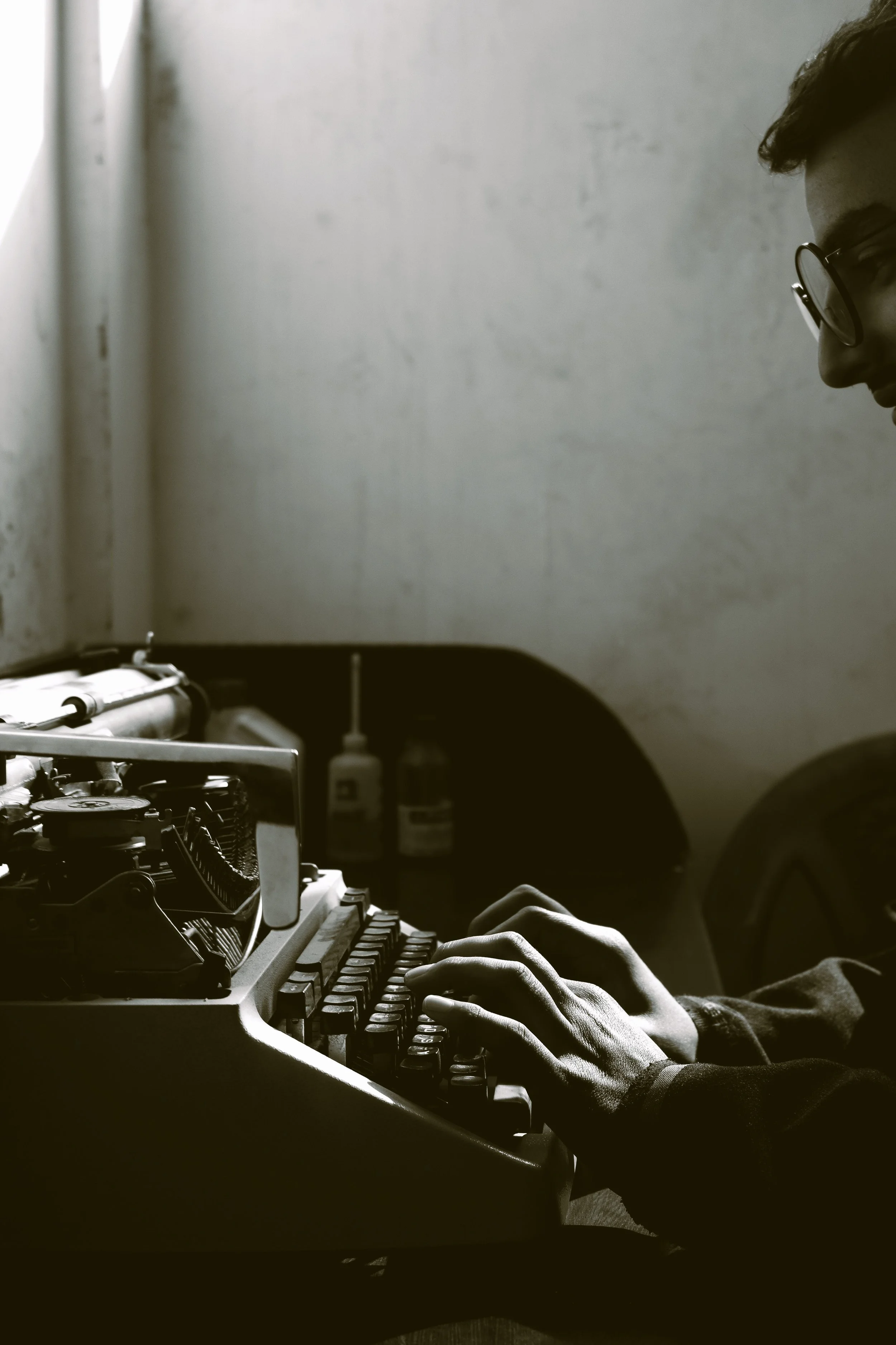 Person wearing glasses typing on an old typewriter in a dimly lit room.