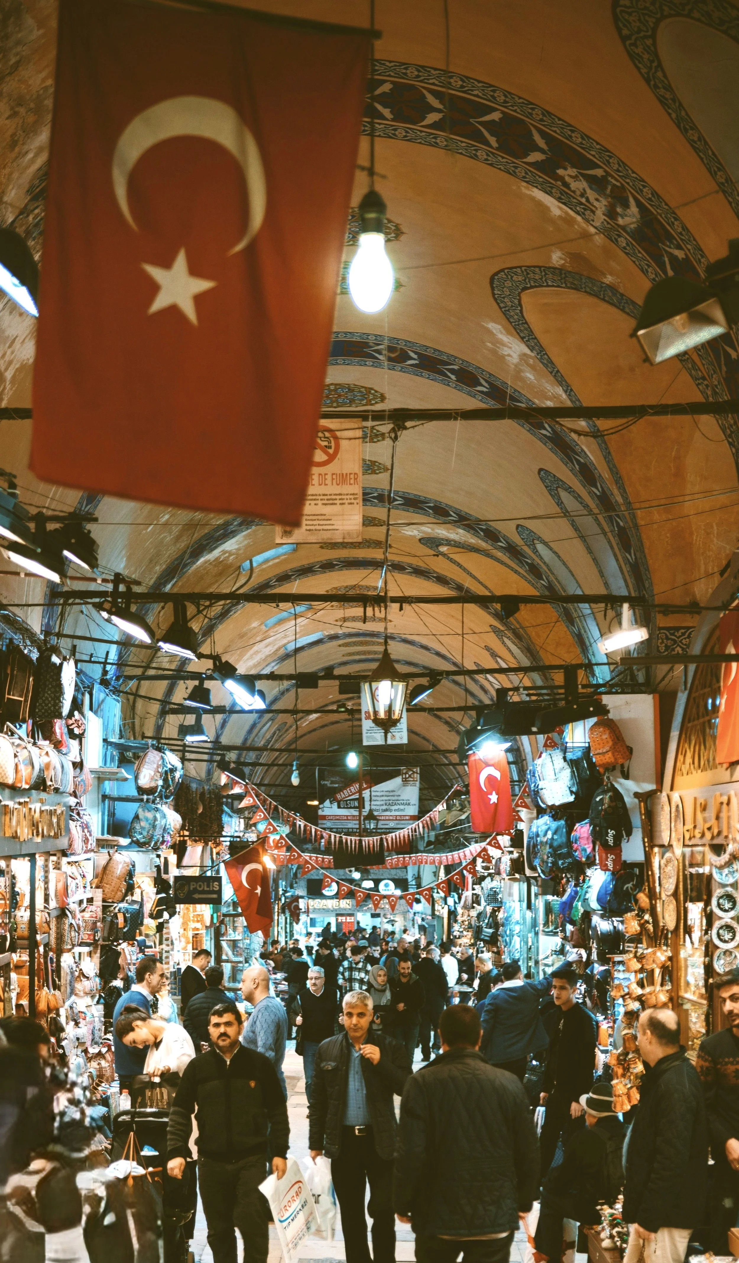 Grand Bazaar corridor with a large Turkish flag hanging above and visitors walking through, Istanbul.