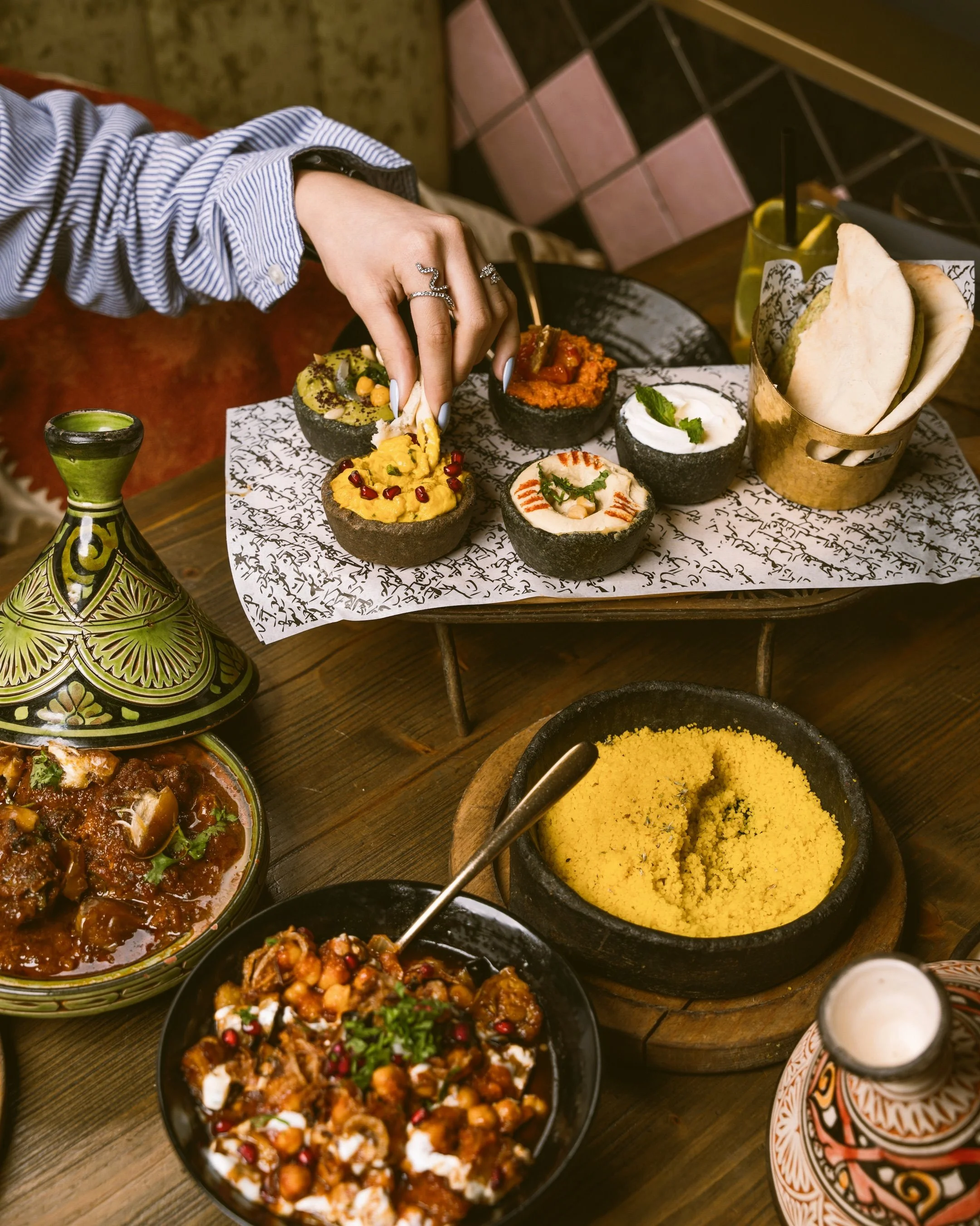 Hand reaching for small bowls of Moroccan dishes, including couscous and salads, spread on a table, Marrakech.
