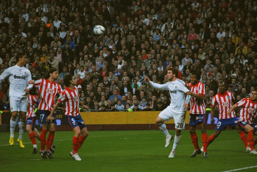 Real Madrid and Atlético Madrid players competing for the ball during a Madrid derby match in a packed stadium