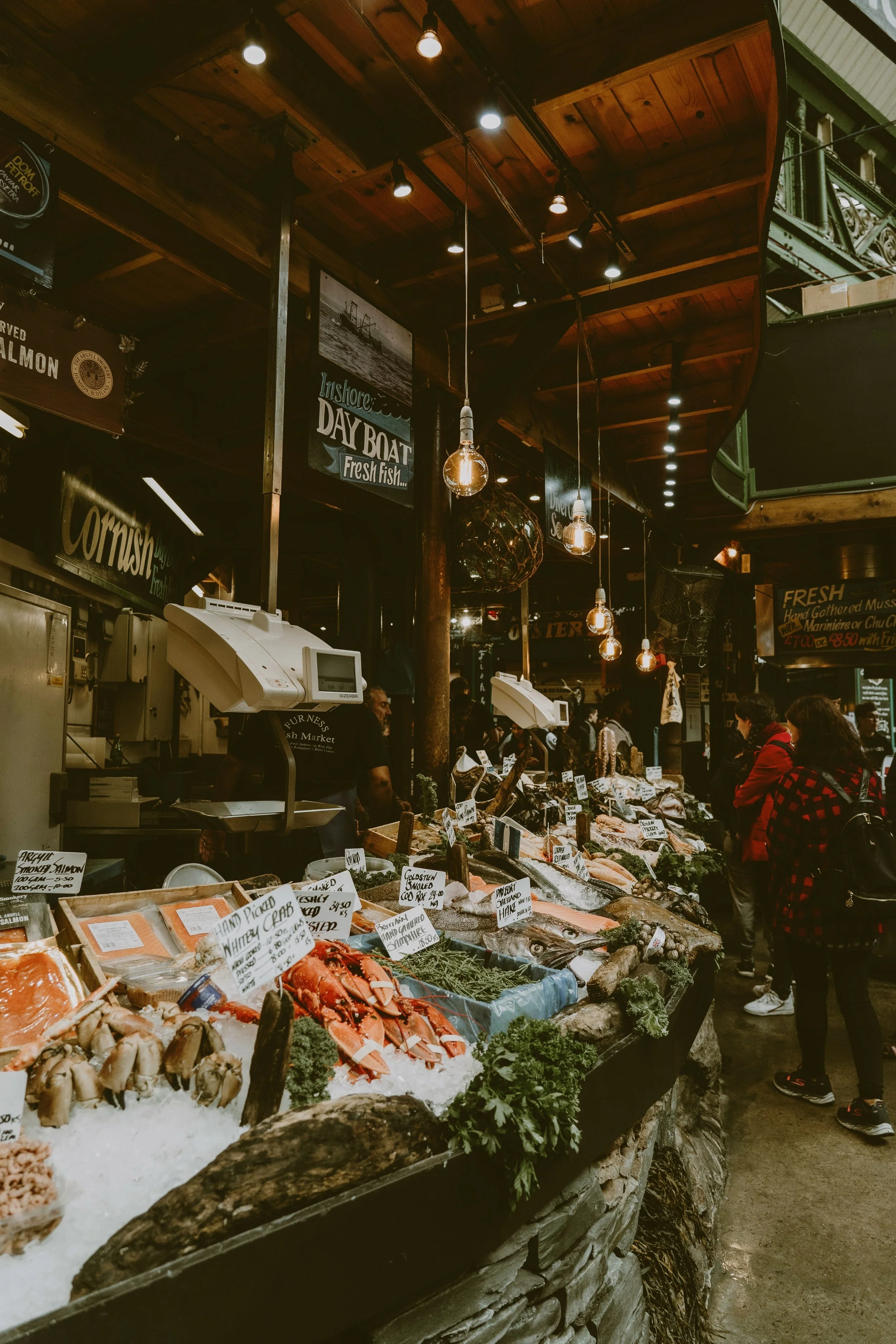 Covered market stalls piled with fresh produce under string lights, Borough Market, London.