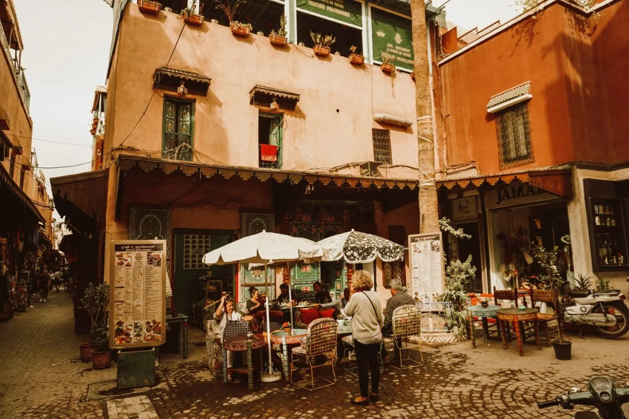 Café terrace with white umbrellas and tables in front of terracotta buildings, Marrakech.