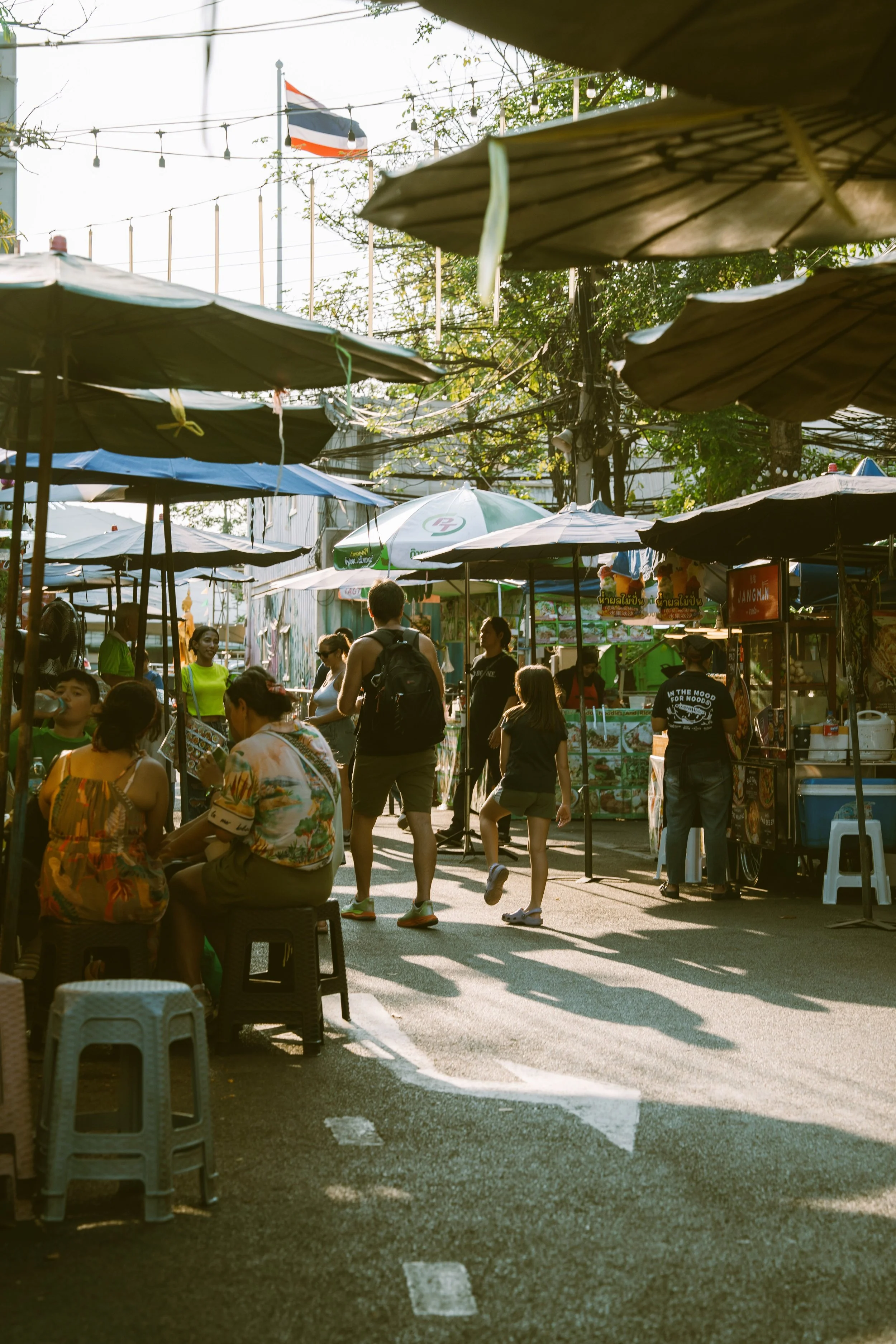 Sunlit lane at Chatuchak Market with plastic stools and awnings over the stalls, Bangkok.