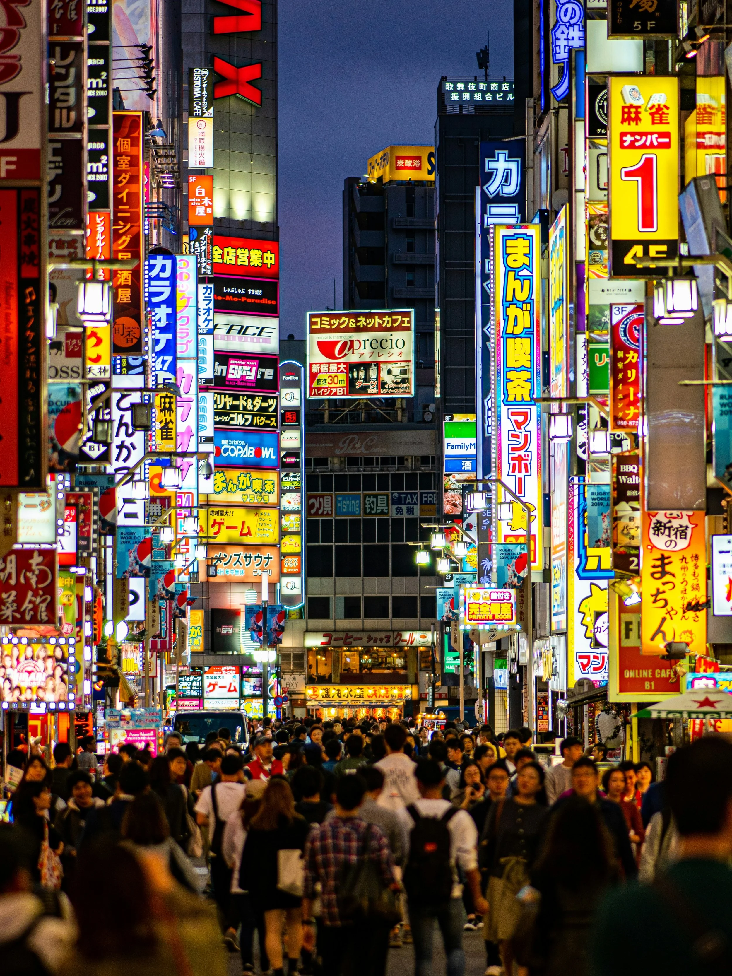 Crowded Kabukichō street at dusk lined with colorful neon signs and billboards, Shinjuku, Tokyo