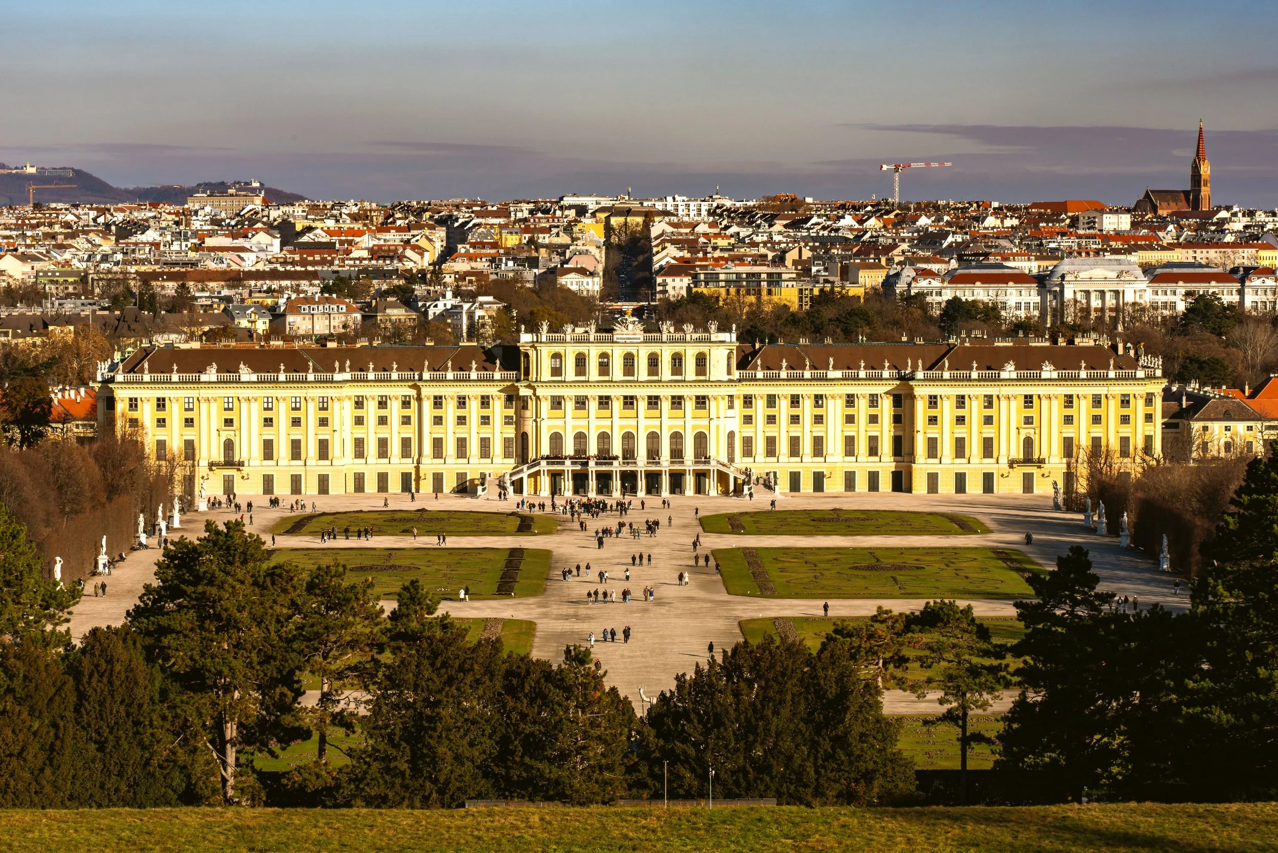 Schönbrunn Palace with its yellow facade and gardens seen from above, with the city skyline behind, Vienna.