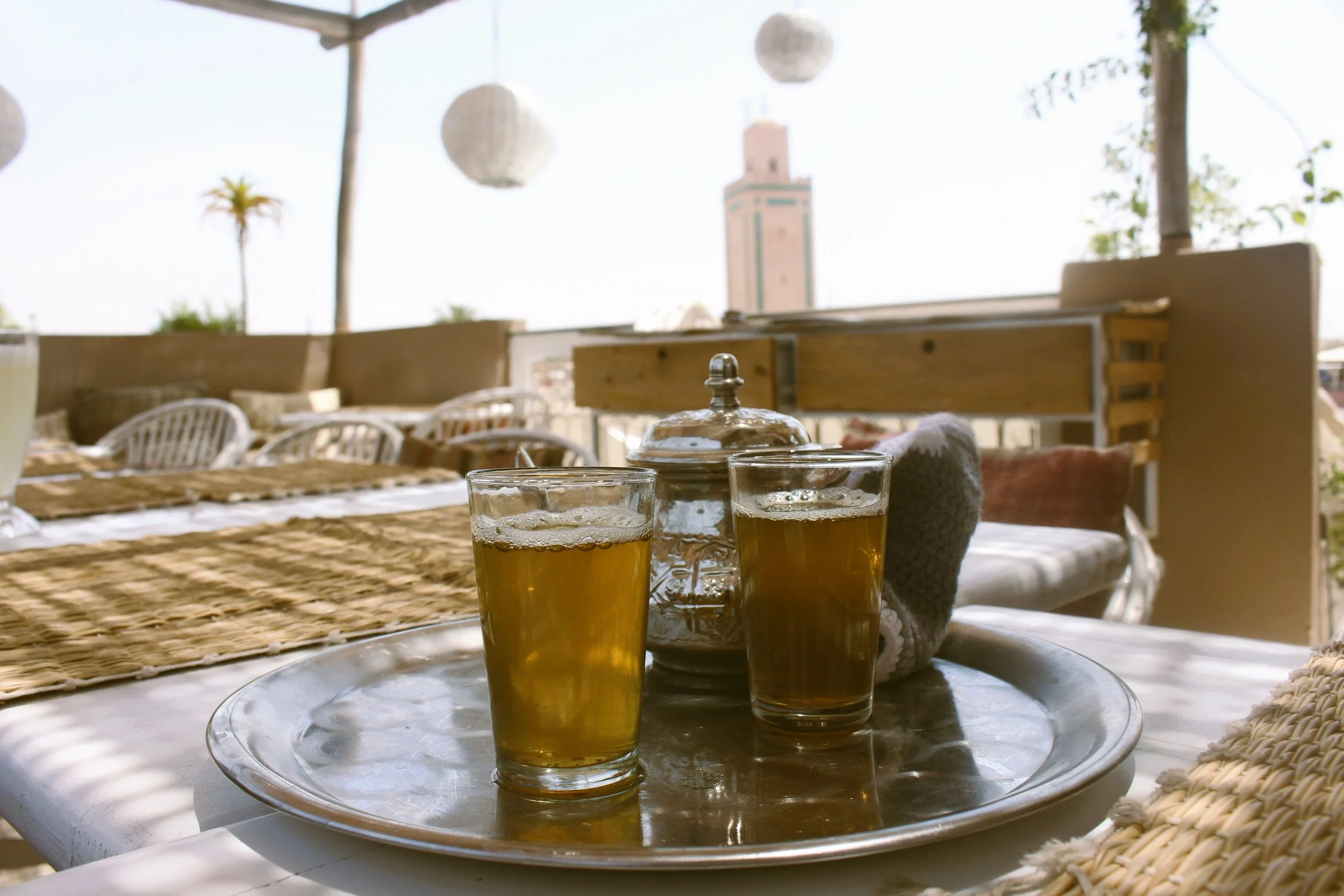 Two glasses of mint tea on a tray on a terrace with a minaret in the background, Marrakech.